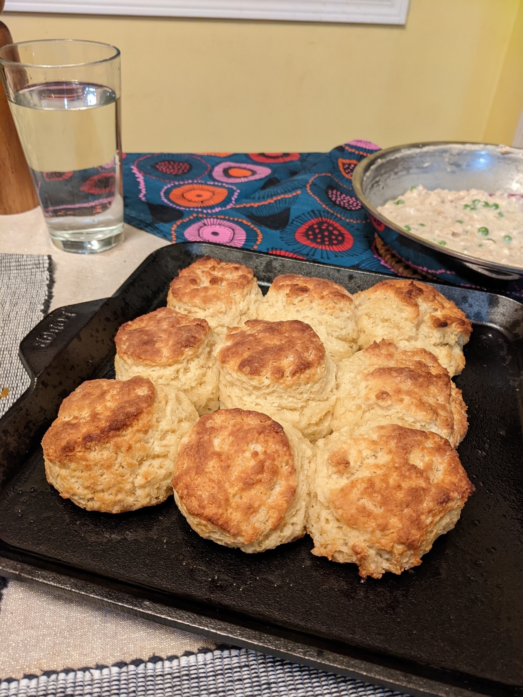 Nine golden topped biscuits baked touching on a cast iron griddle, with a pan of creamed tuna