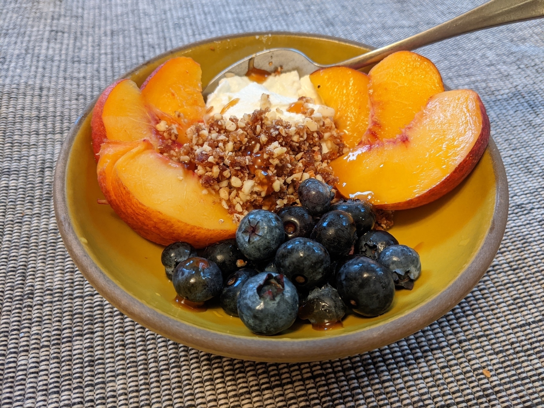 bowl with peach slices, blueberries, almond date gravel, Greek yogurt and honey