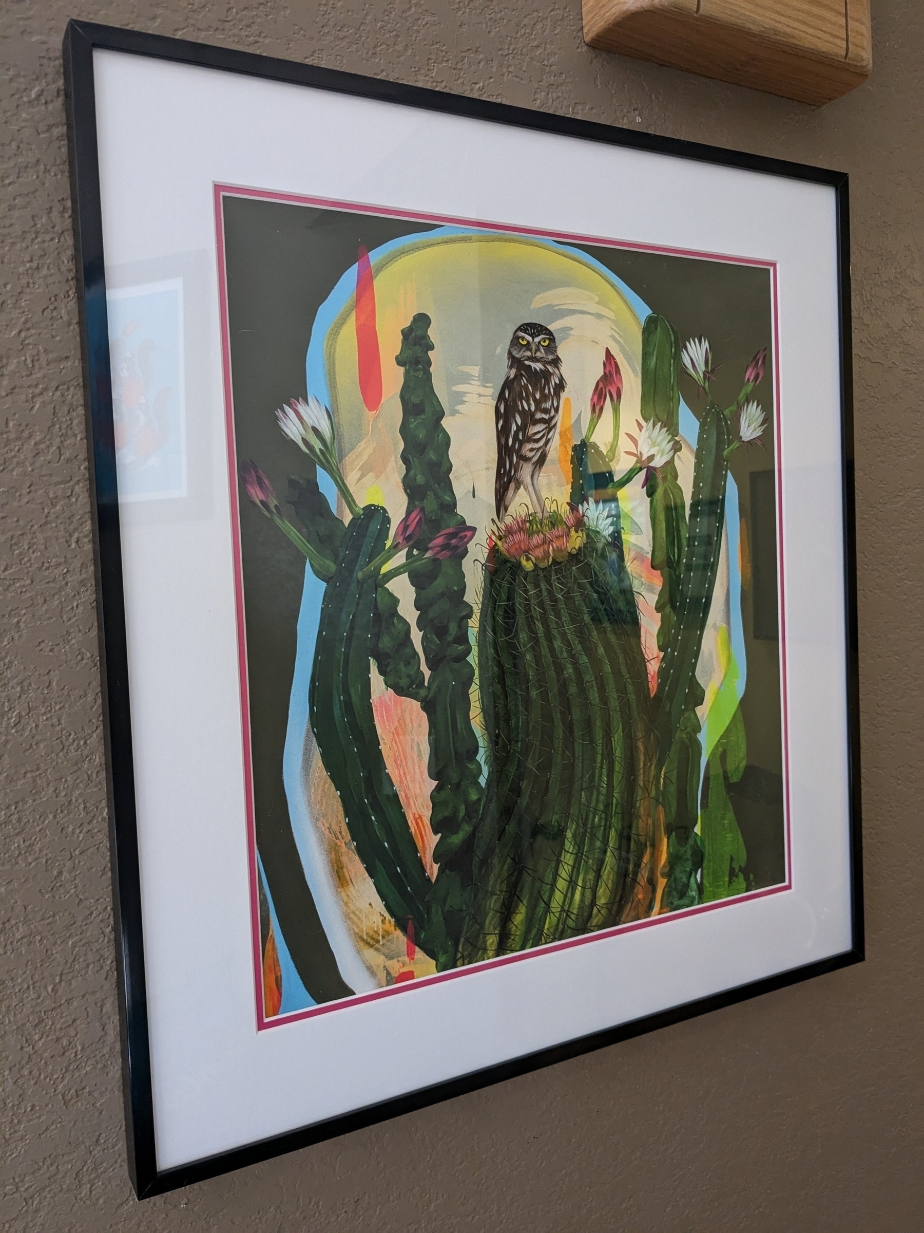 framed print of a colorful owl and cactus painting with thin shiny black frame and double mat, white on top and a thin hot pink mat around the print