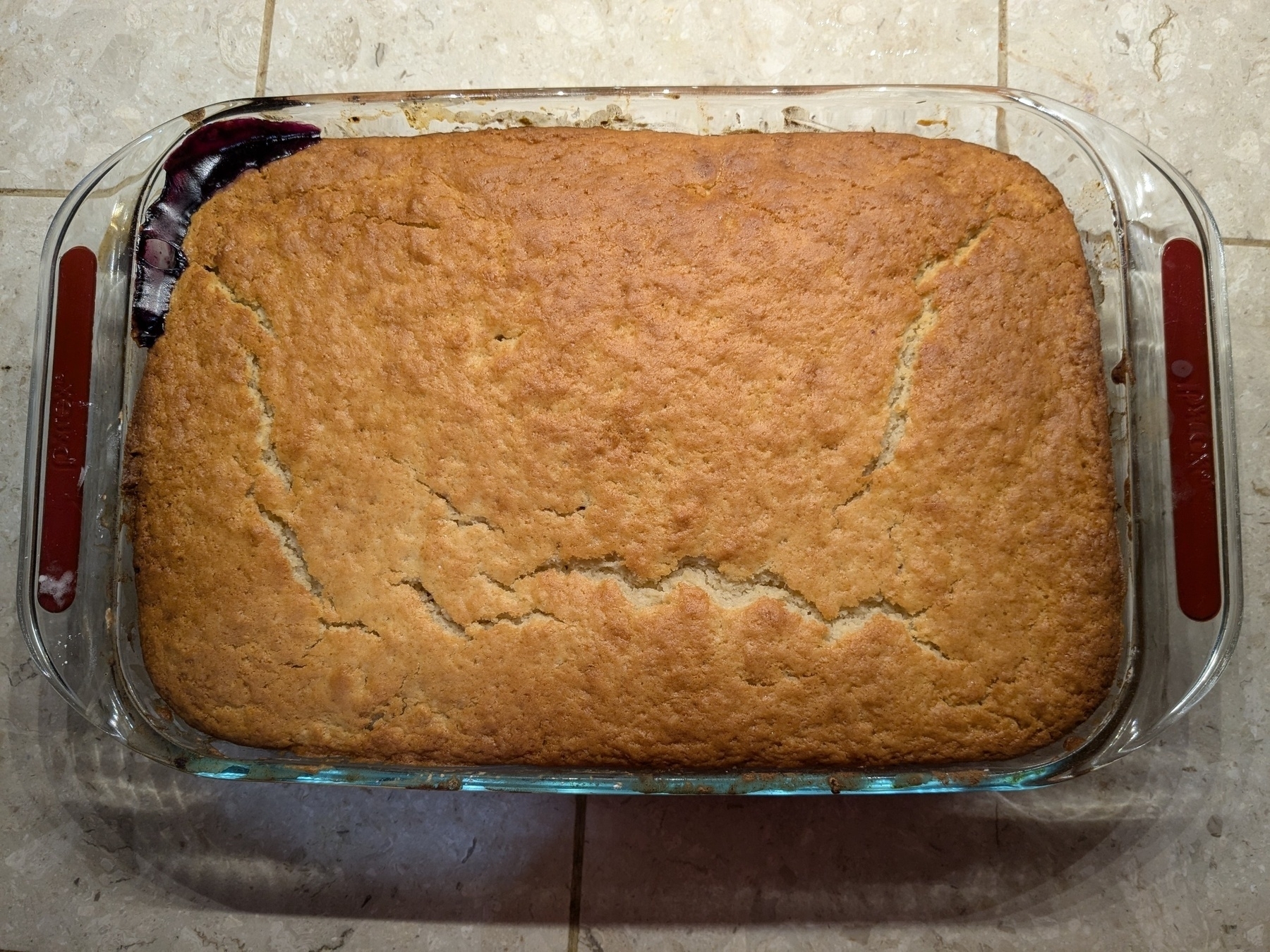 smooth topping pyrex of baked cobbler, just a bubbling of fruit on one corner 