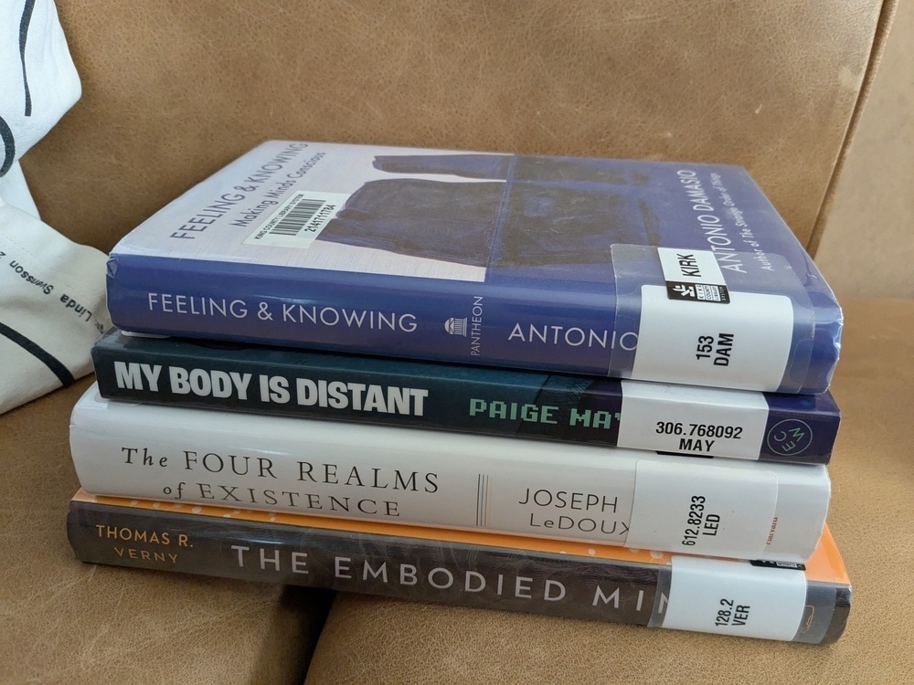 stack of 4 library books on thinking, consciousness, and embodiment; three nonfiction, one memoir