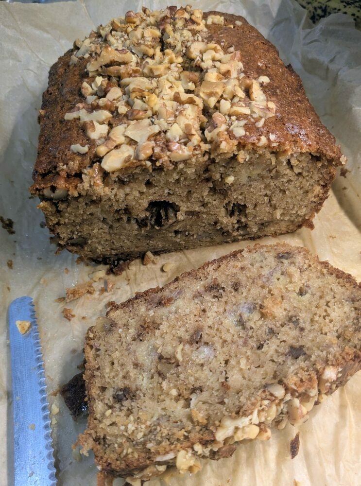loaf of banana nut bread cut open with a slice laying in front, a big stripe of chopped nuts along the top