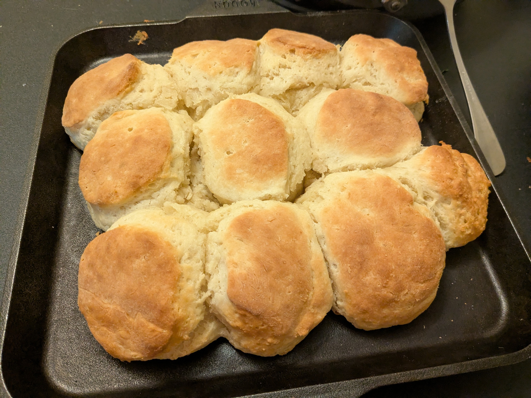 three rows of biscuits, touching, on a cast iron square skillet with golden brown tops 