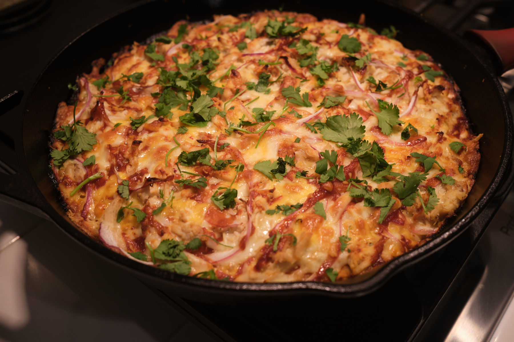 in a cast iron pan, a fresh out of the oven pan-crust pizza topped with homemade bbq sauce, Tillamook spicy mexican blend cheese, shredded chicken, sliced red onions, and fresh cilantro