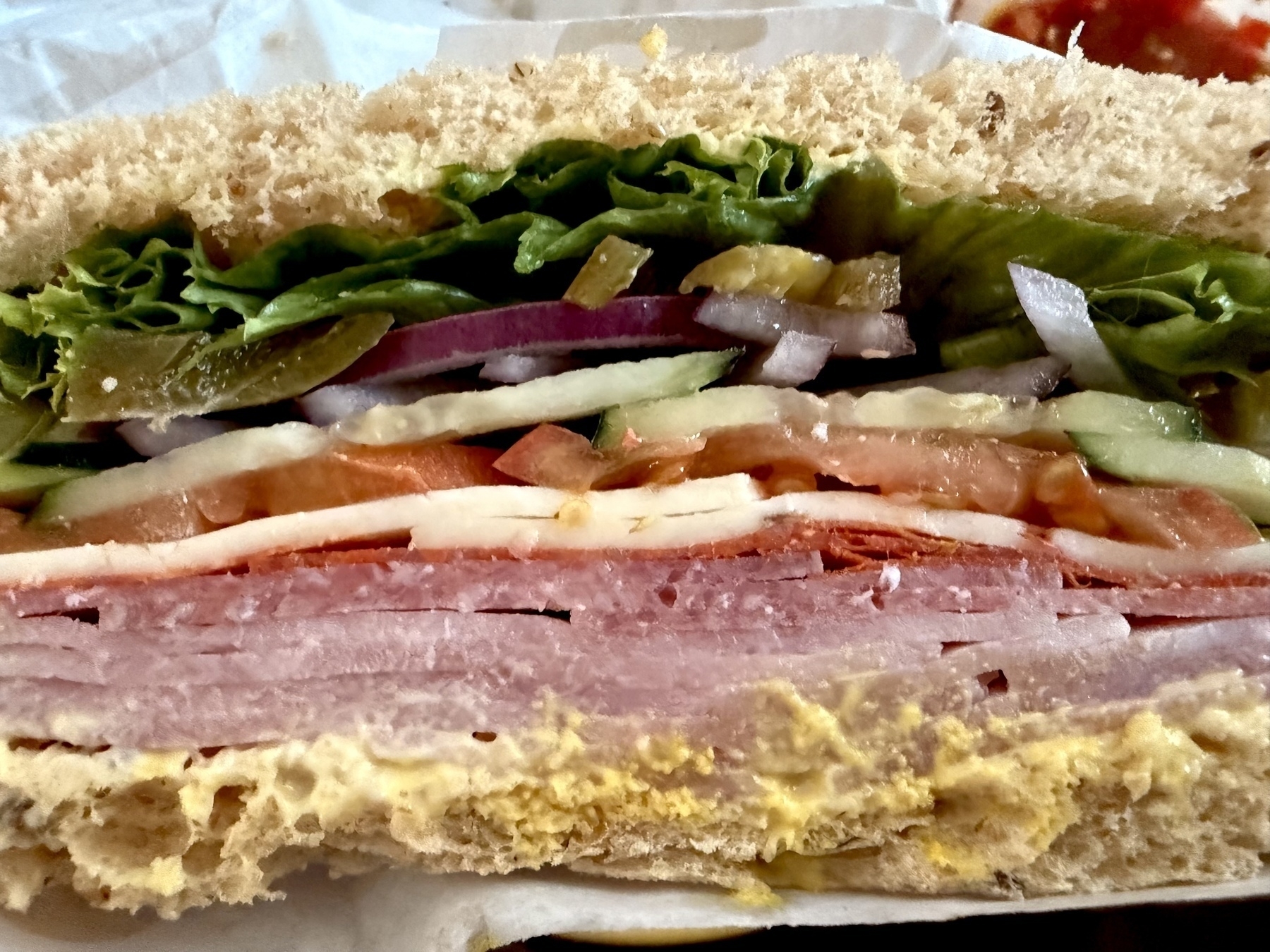 A deli sandwich showing layers of meat, cheese, and vegetables. 