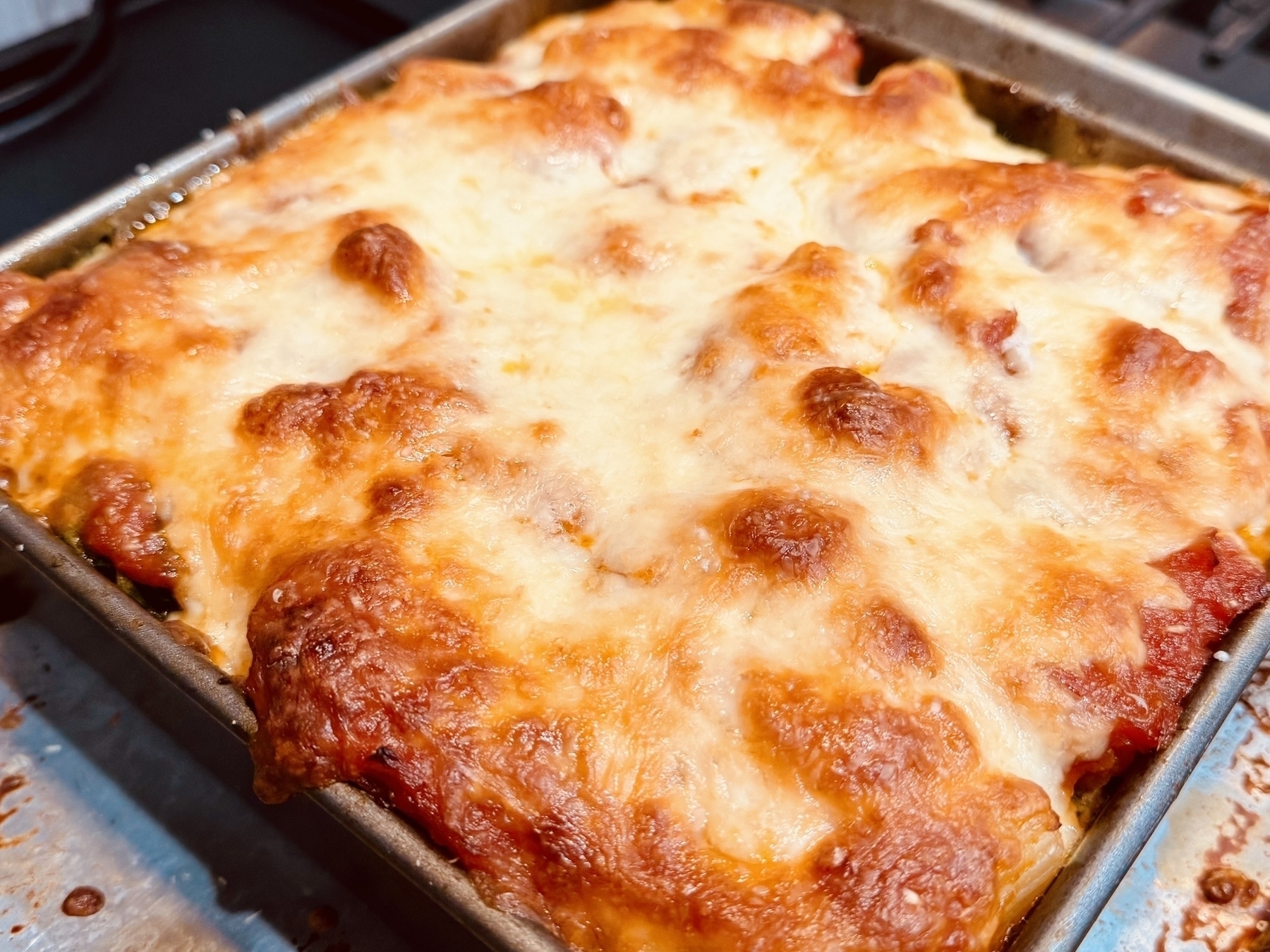 A square baking pan of baked ziti, with the cheese and golden brown on top. 