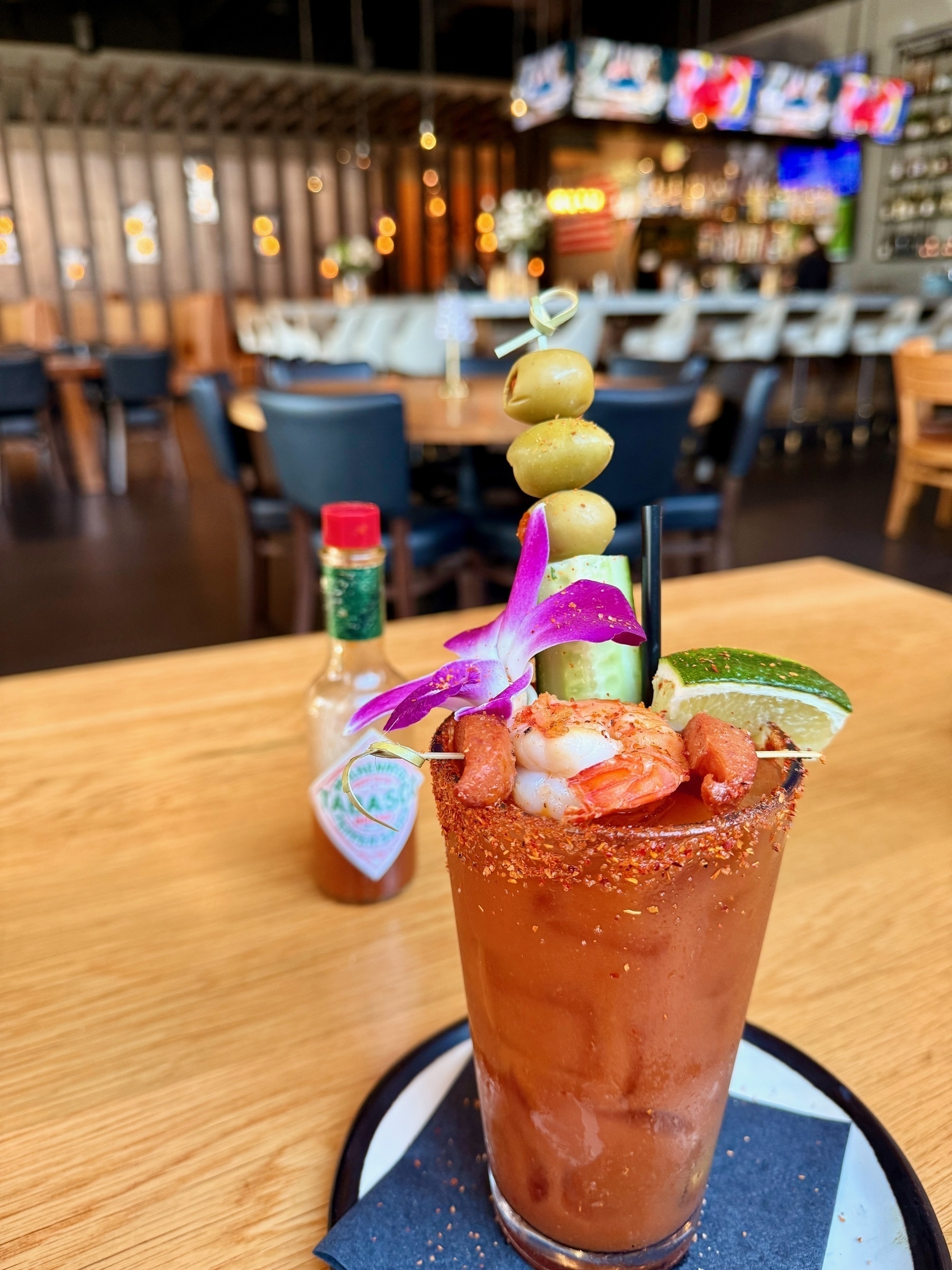 A bloody mary garnished with a cucumber, three olives, a lime, a shrimp tail and two slices of cajun sausage. 