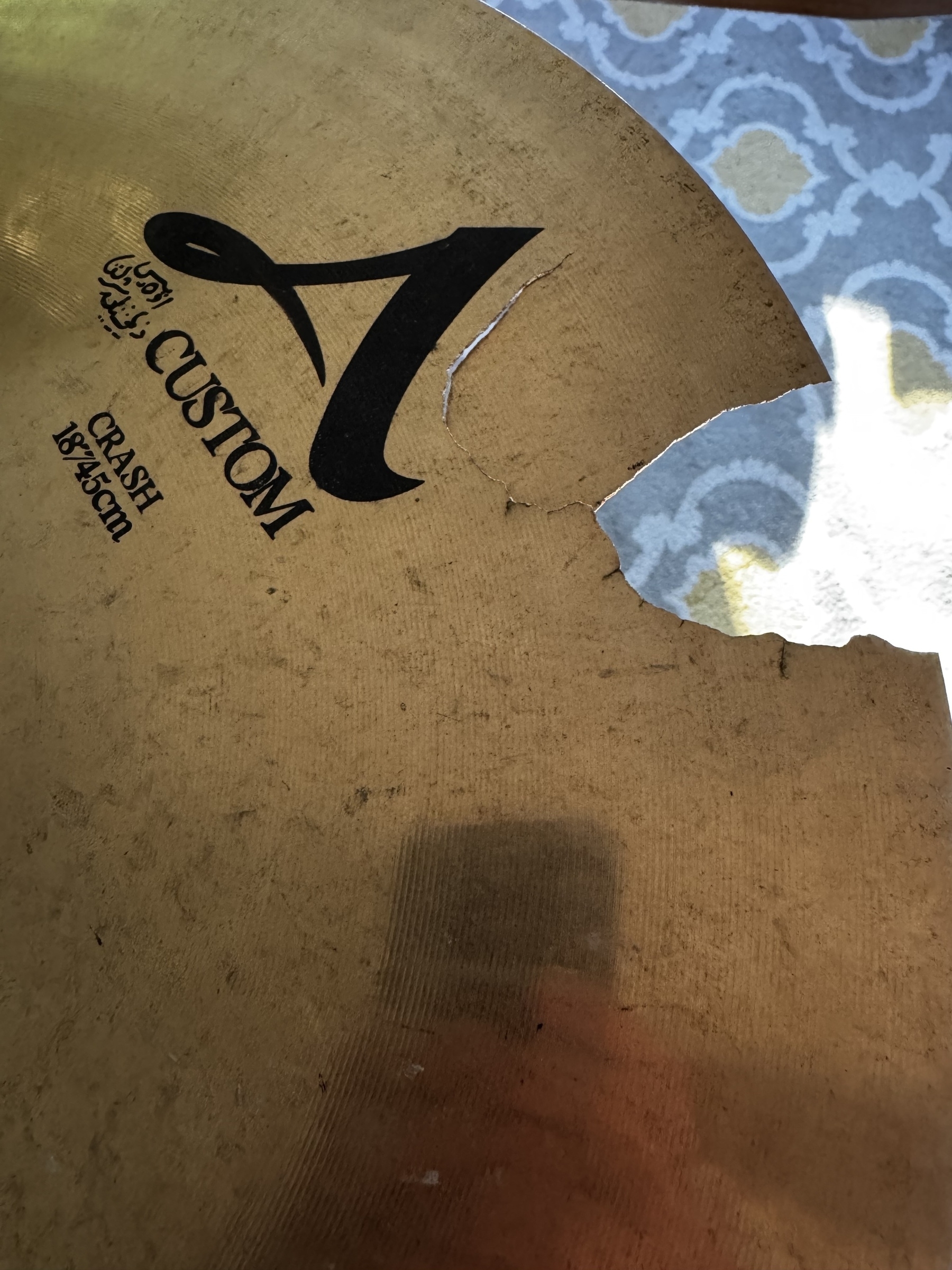 A broken Zildjian crash cymbal with the label "A Custom Crash" and a patterned carpet in the background.