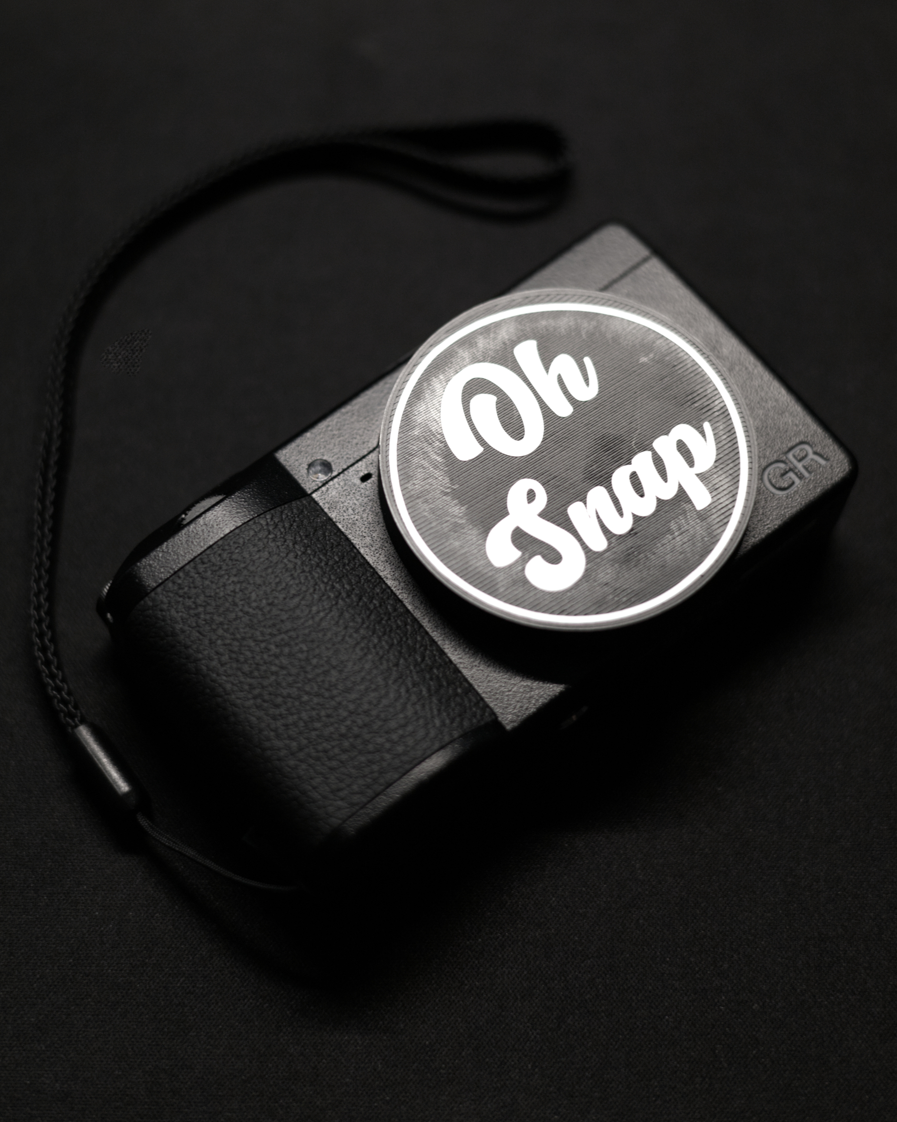 My black Ricoh GR III with a black 3D printed Lens Cap that says 'Oh Snap' in white vinyll lettering