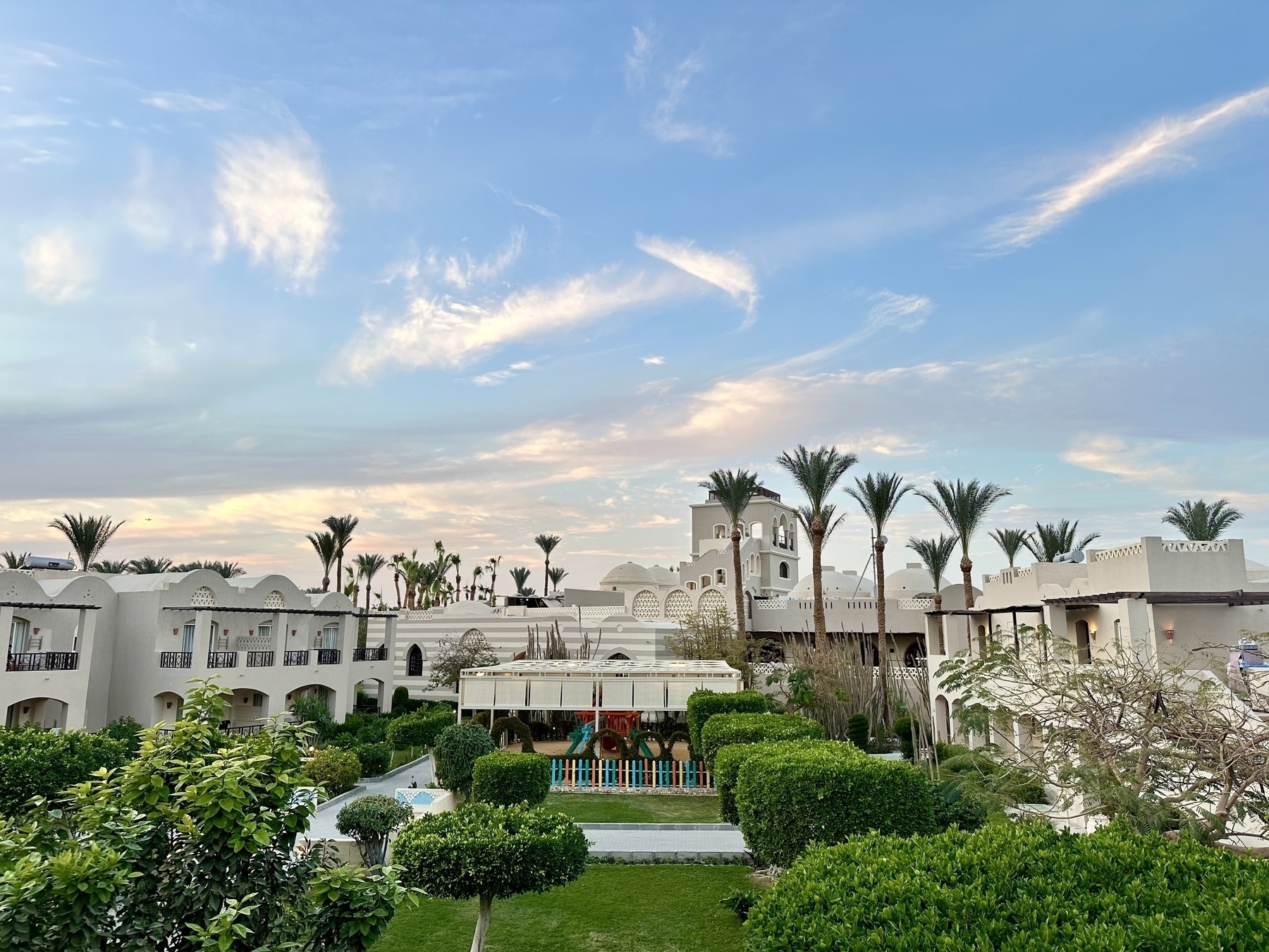 Sunset in Makadi Bay, Egypt. A lush garden  in front of a tower. Palms in the background and a beautiful sunset with some light clouds.