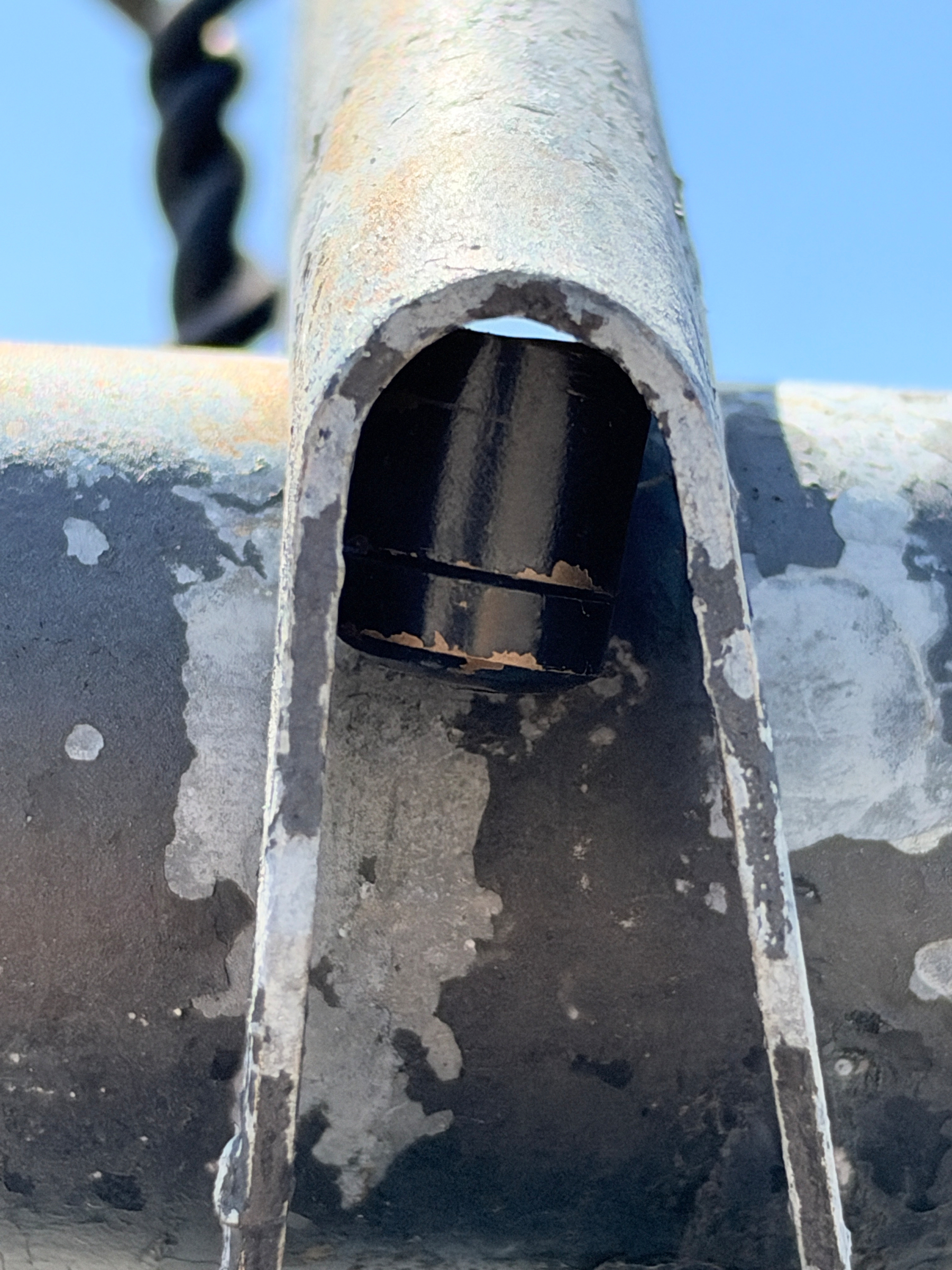 A close-up view of a weathered metal structure with peeling paint, showing part of a bolt or fastener inside a hollow section.