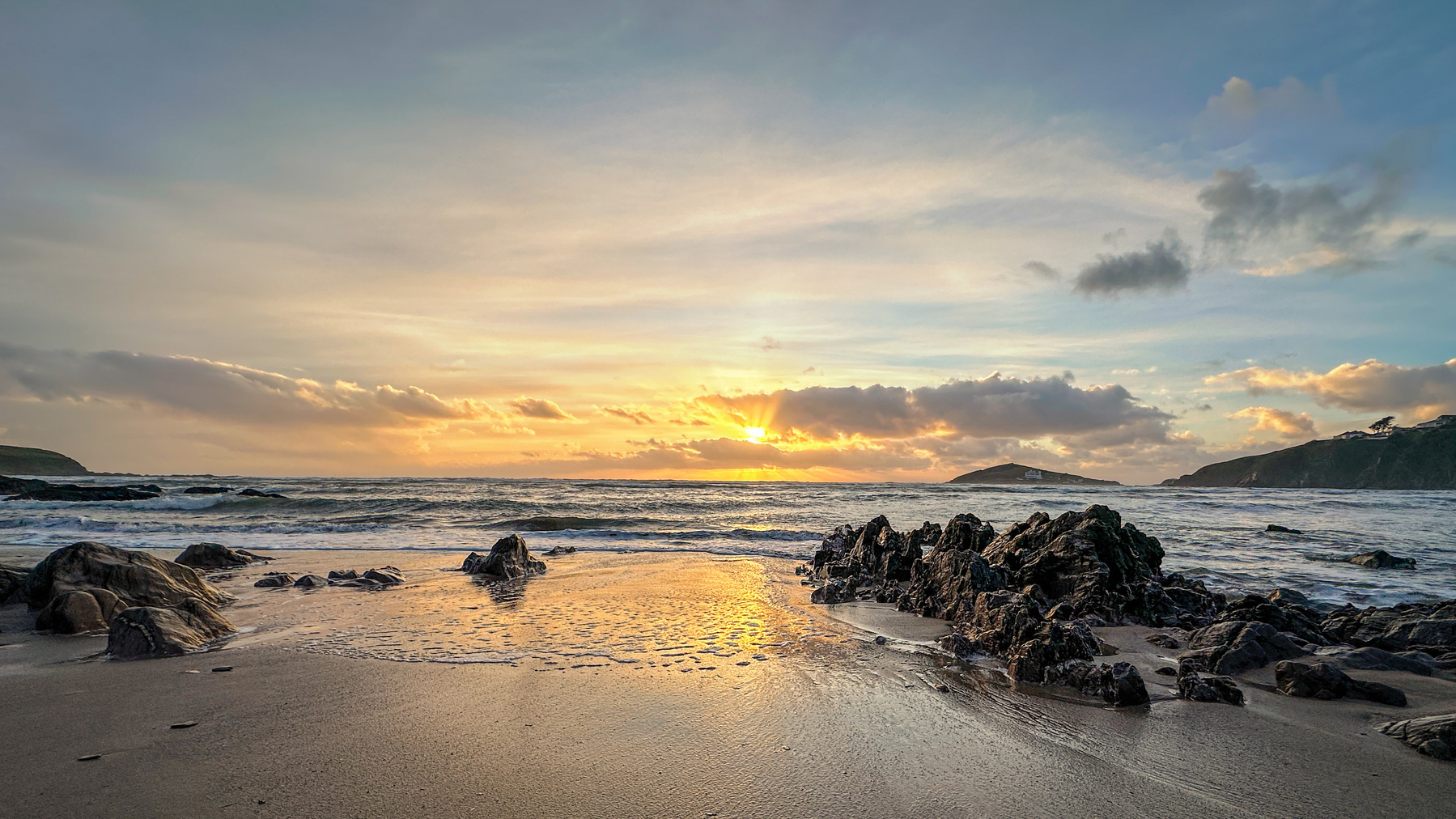 A tranquil beach scene features rocky shores and gentle waves under a colorful sunset sky.