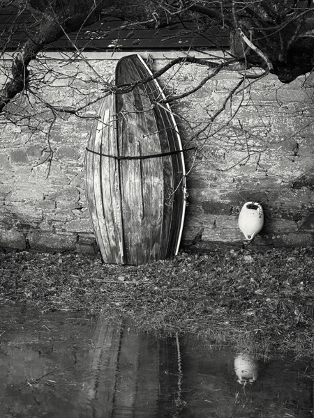 A black and white photograph of a rowing boat against a stone wall