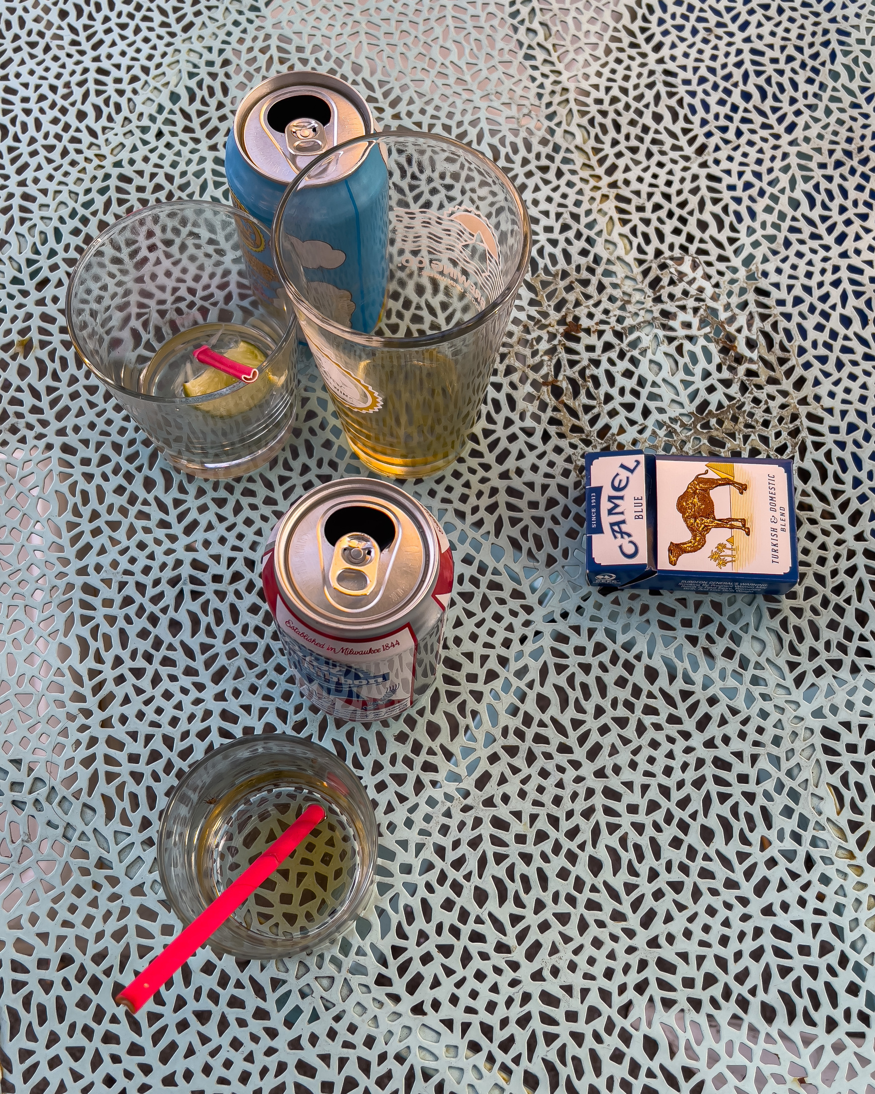 Glasses, cans and cigarette pack on a metal mesh table.