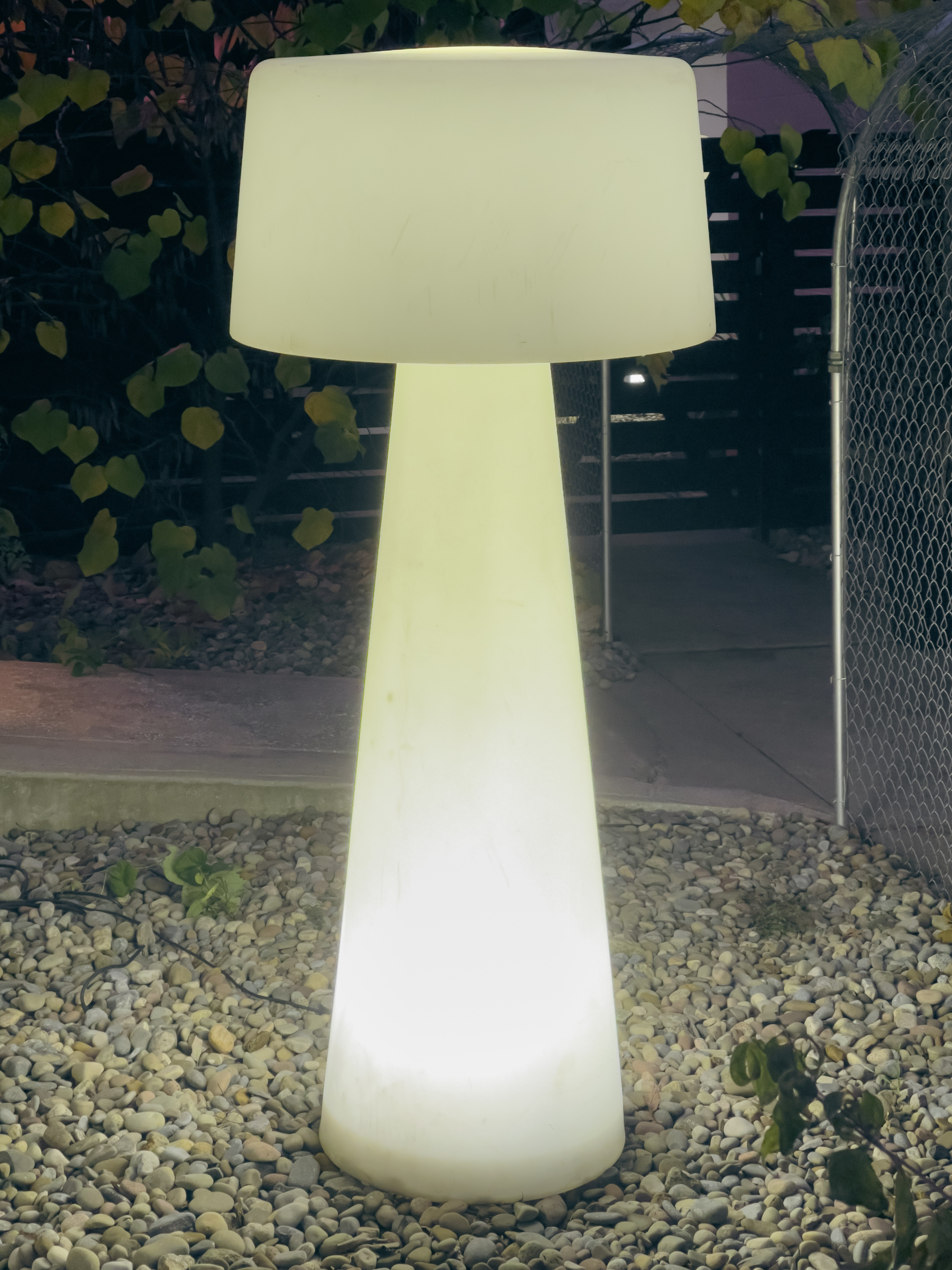 Large outdoor light fixture in shape of modern lamp and glowing in early morning.