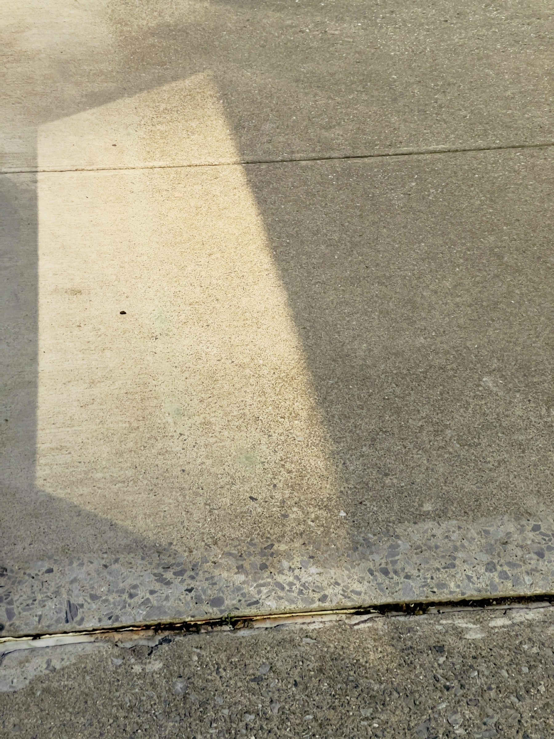Parallelogram of light on concrete sidewalk.