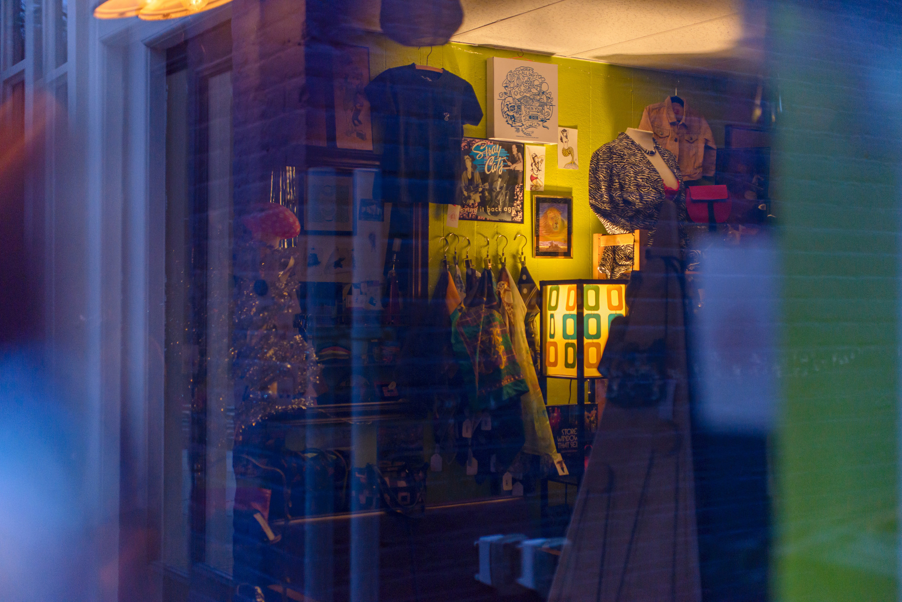 Interior of vintage clothing store with soft glow of table lamp illuminating vintage items and a soft blue light reflected off the window at the left and right edges.