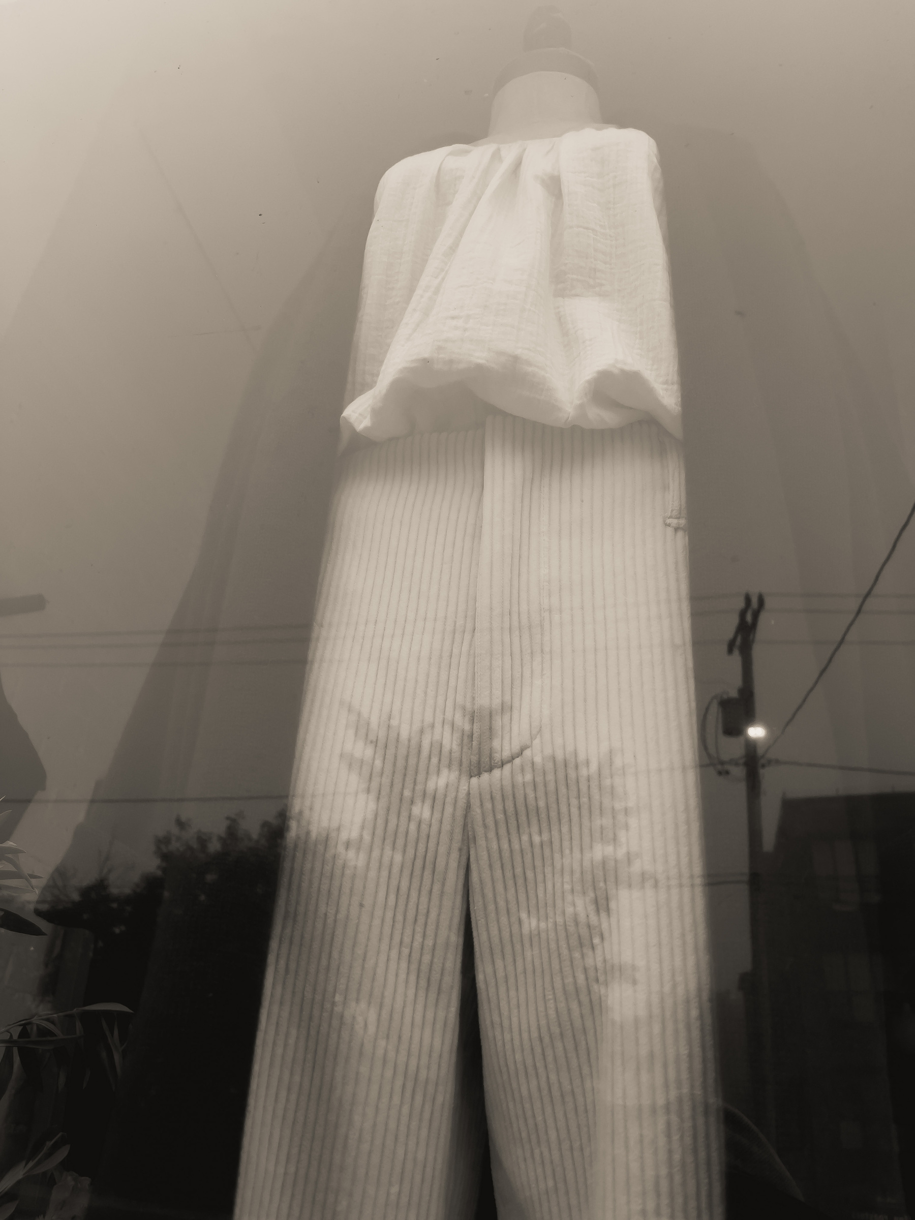 Blouse, pants and long coat on mannequin in shop window.