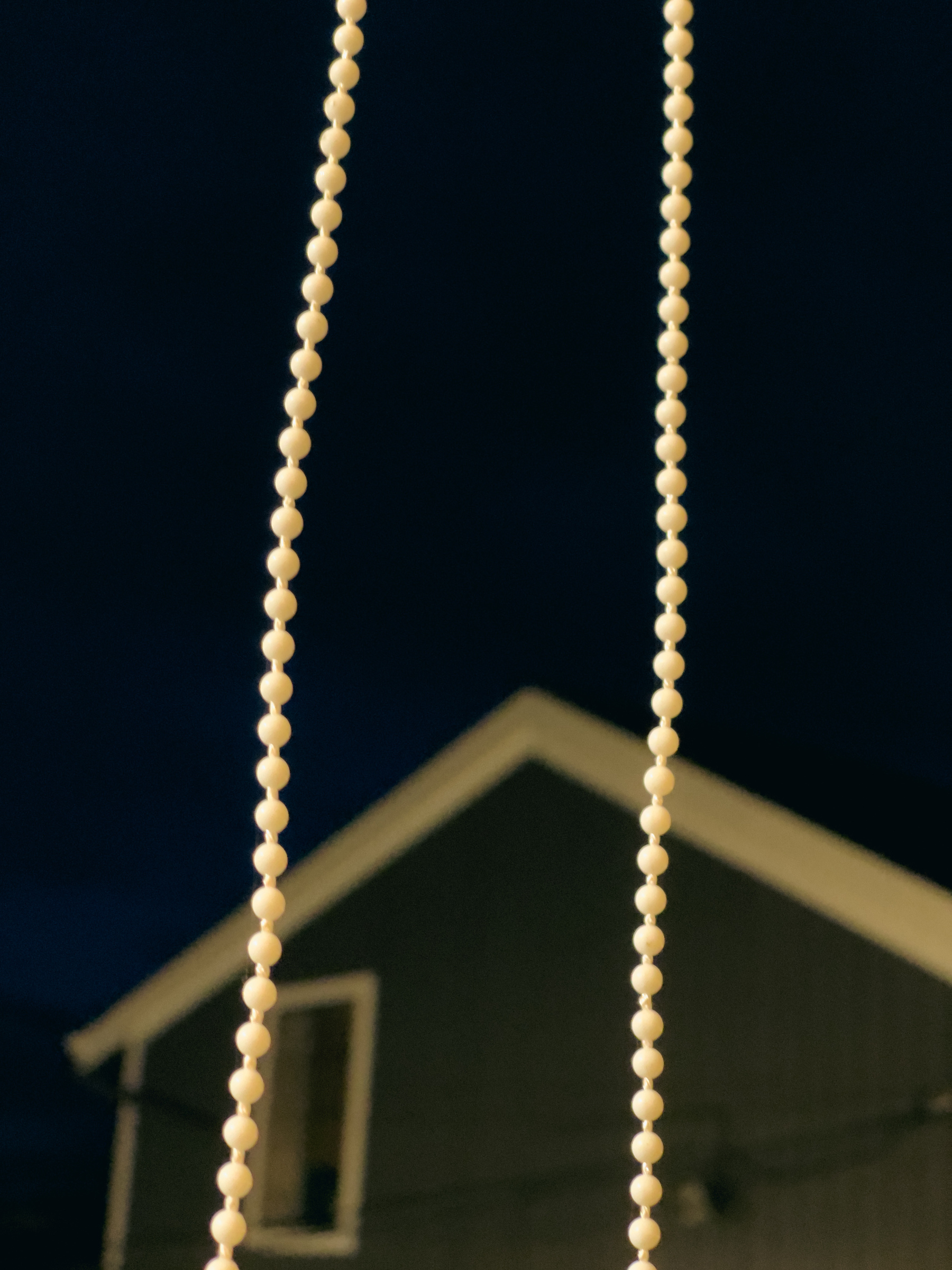 Two strings of beads dangling from top to bottom with house in background.