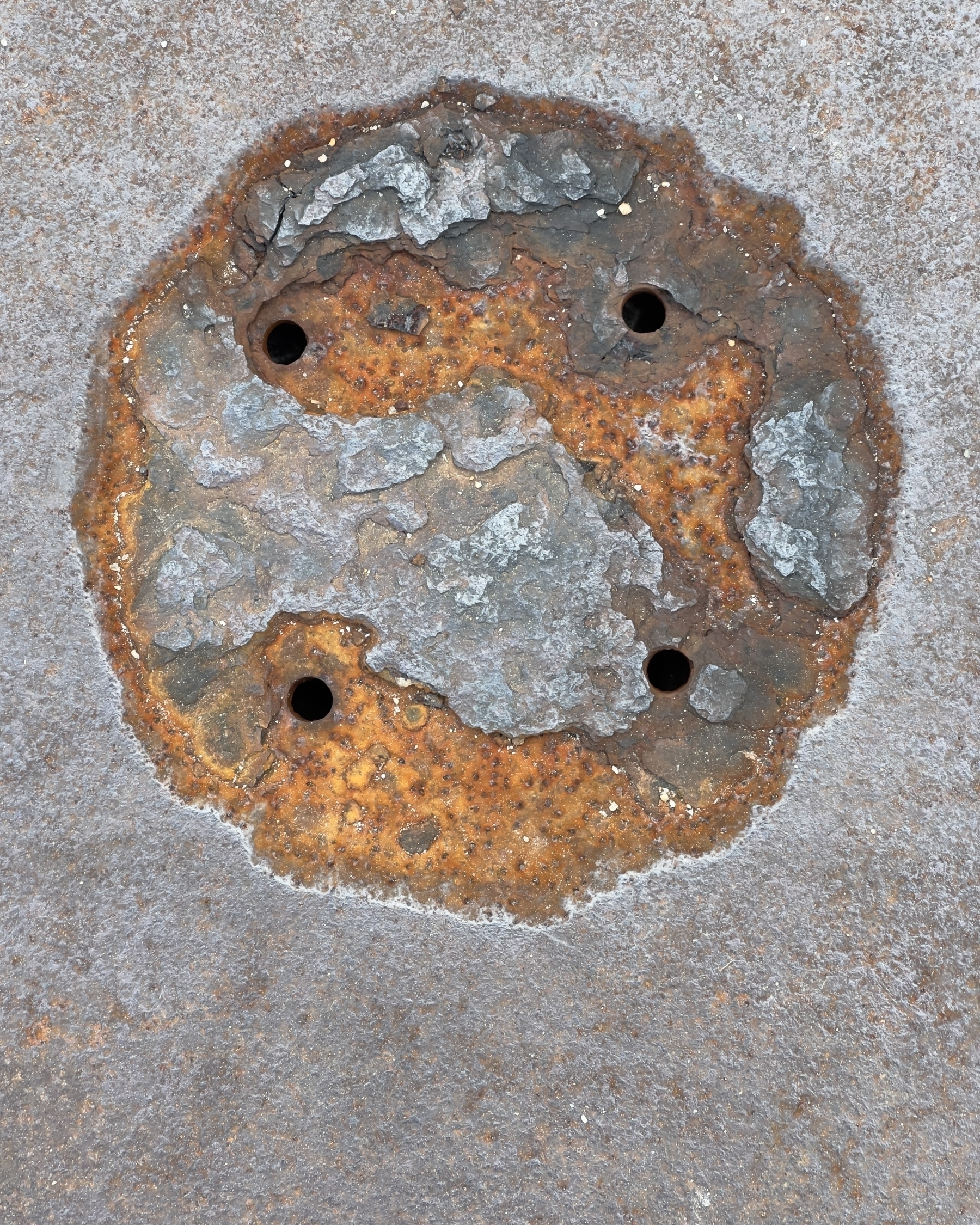 4 small holes in a square pattern in a circular patch of rust in a manhole cover.