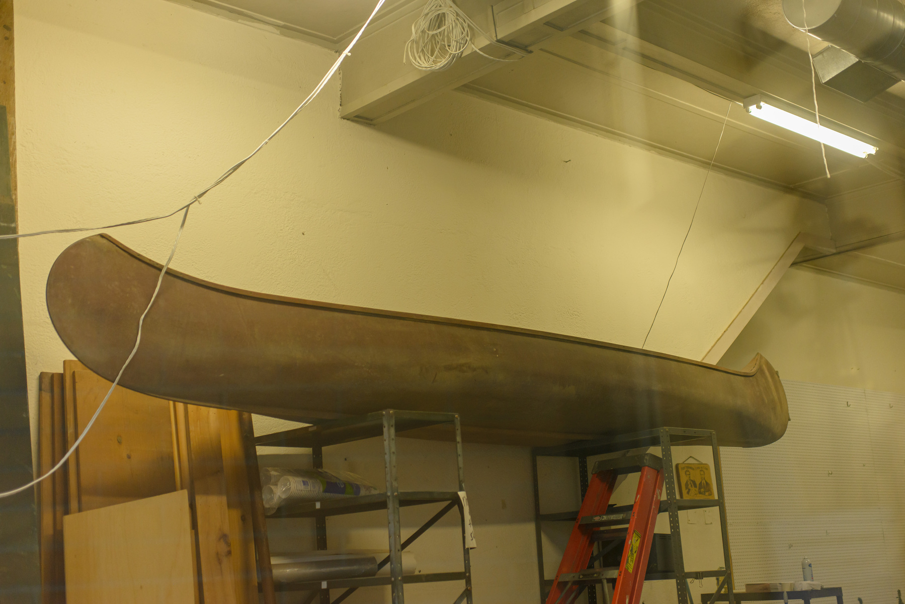 antique canoe siting on top of metal shelving units in a high ceiling space 
