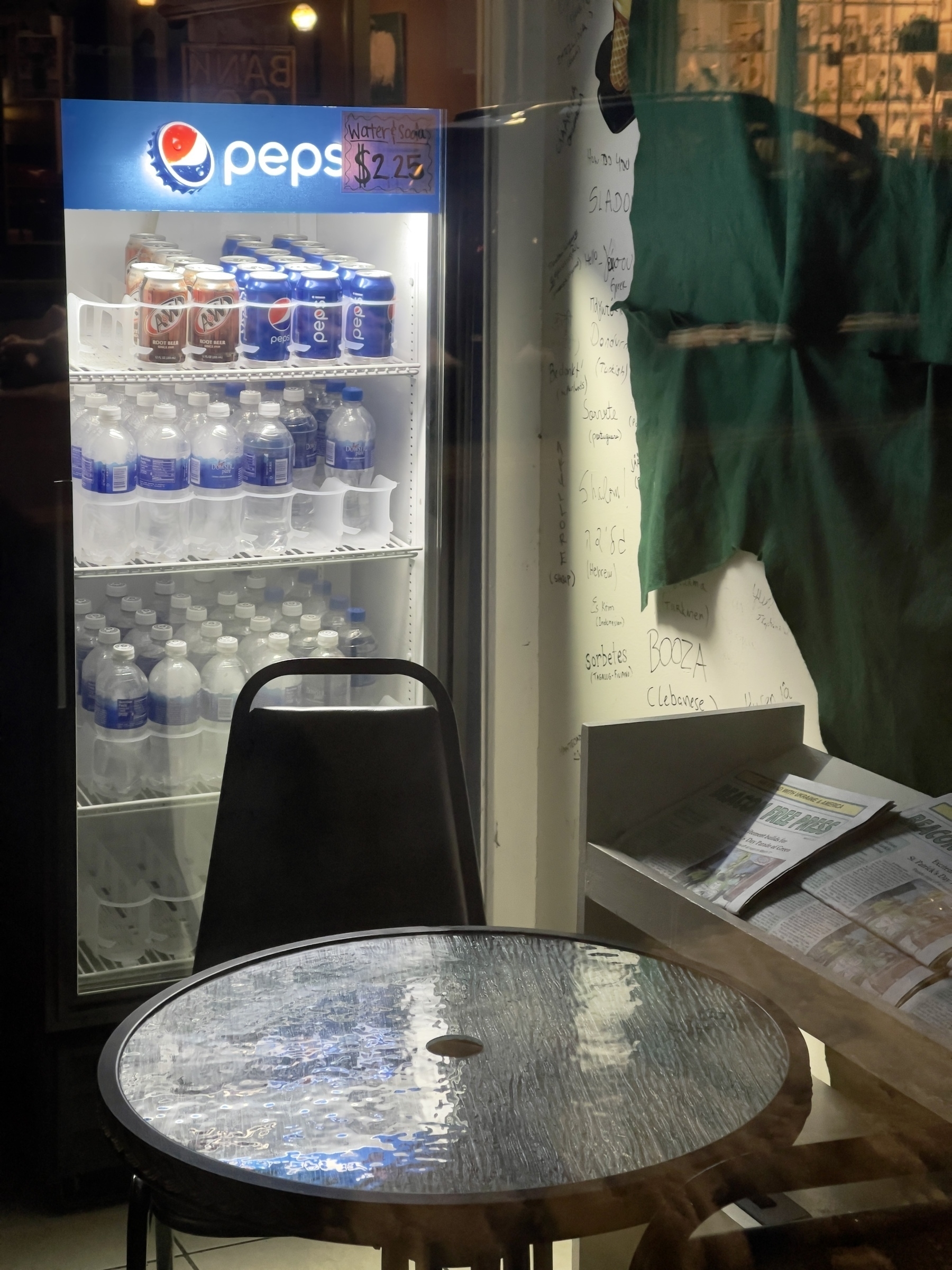 Pepsi refrigerator with table and chair in front of it in a darkened shop.