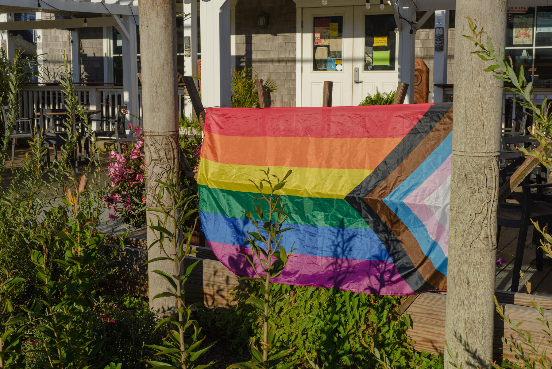 Gay pride flag, hung between two posts with decorative carvings, in front of a building.
