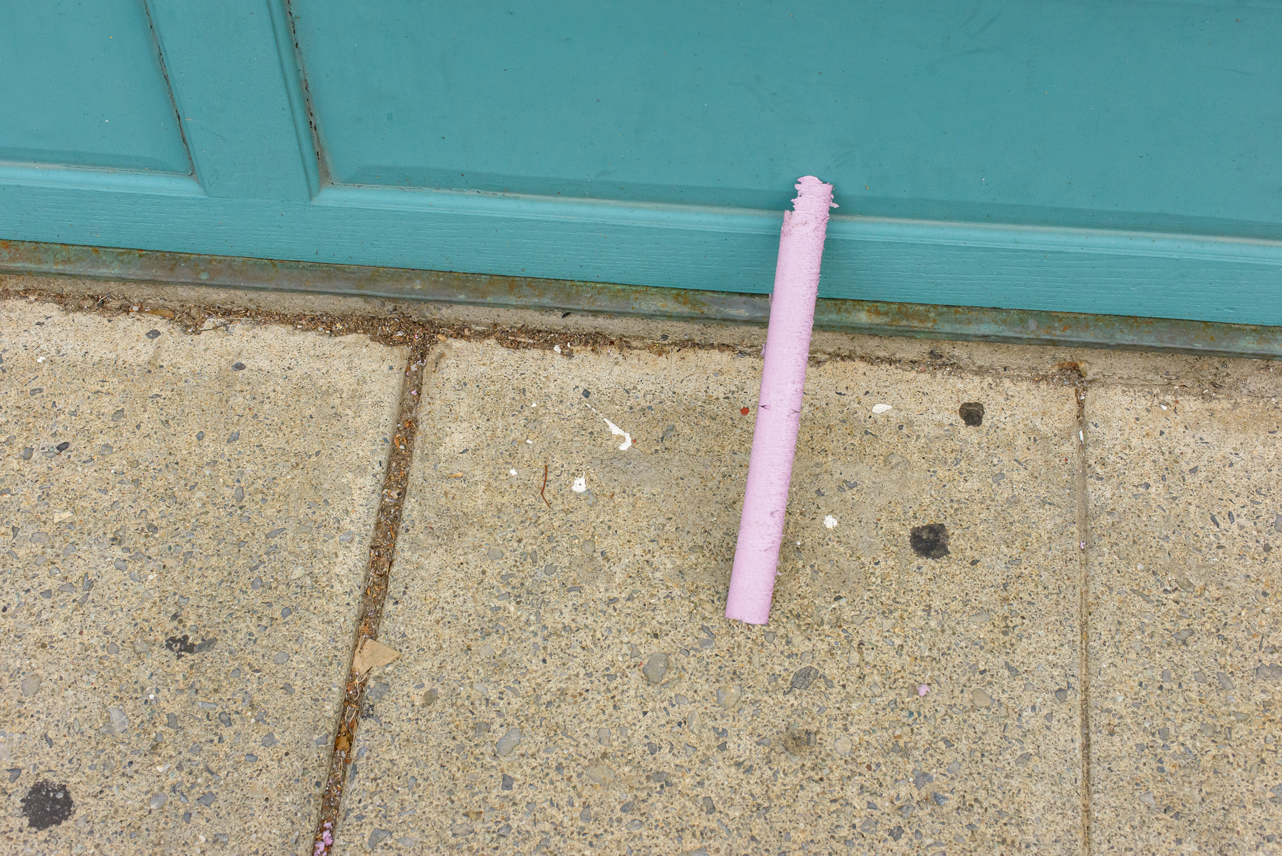 piece of pink tubular debris leaning against a blue/gray wall and the concrete sidewalk