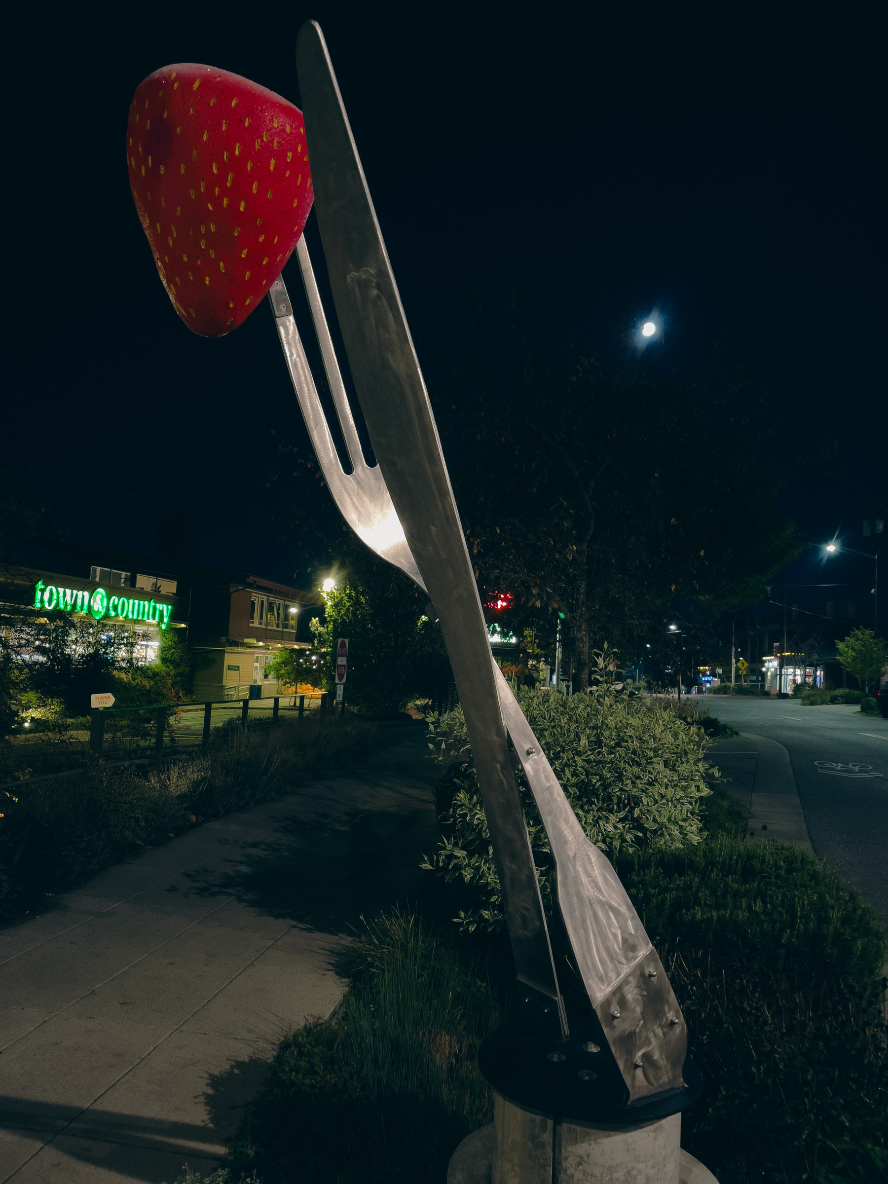 Giant knife and fork sculpture with giant strawberry impaled on top of fork.