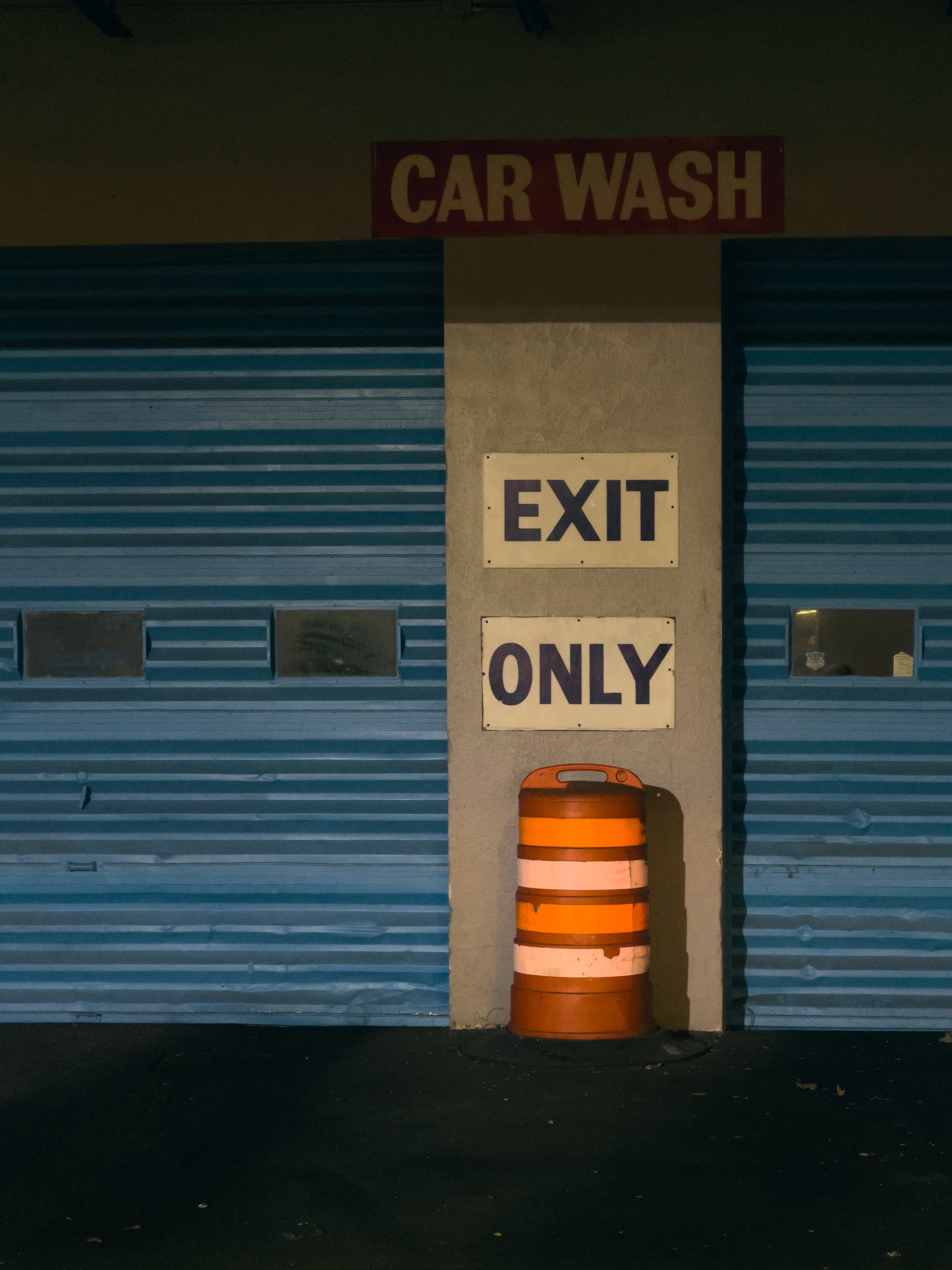 Exit only sign and orange traffic barrel in front of blue garage doors at a car wash.