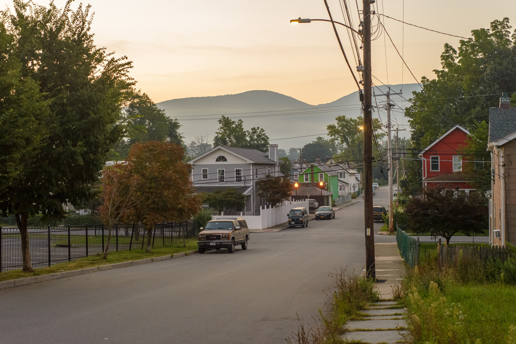 Streetscape with trees, cars, utility wires and mountains in the background. Early morning.