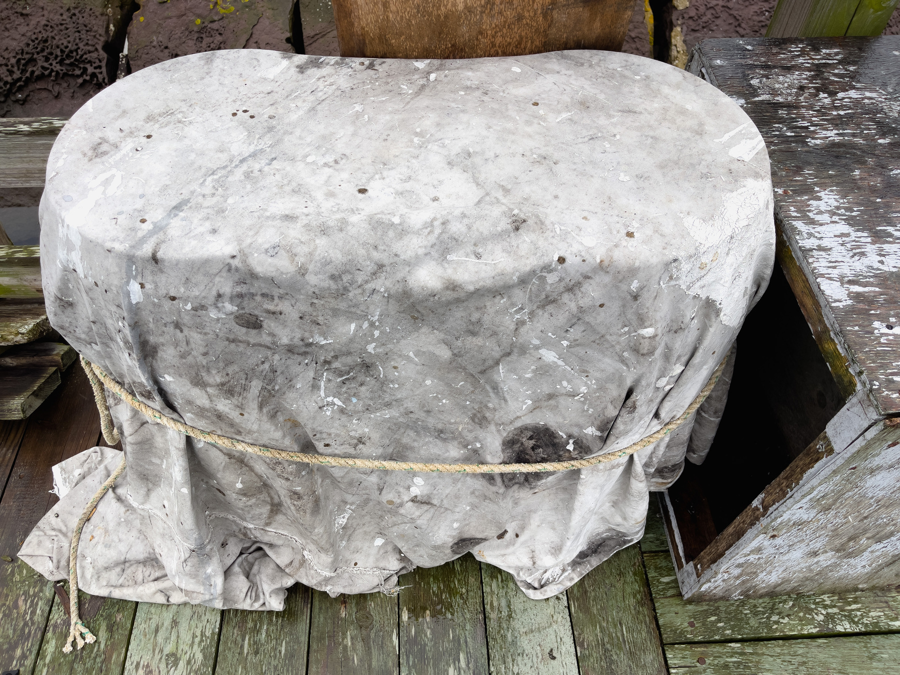 Dirty white tarp over object with rounded ends held on with a rope tied at the middle.