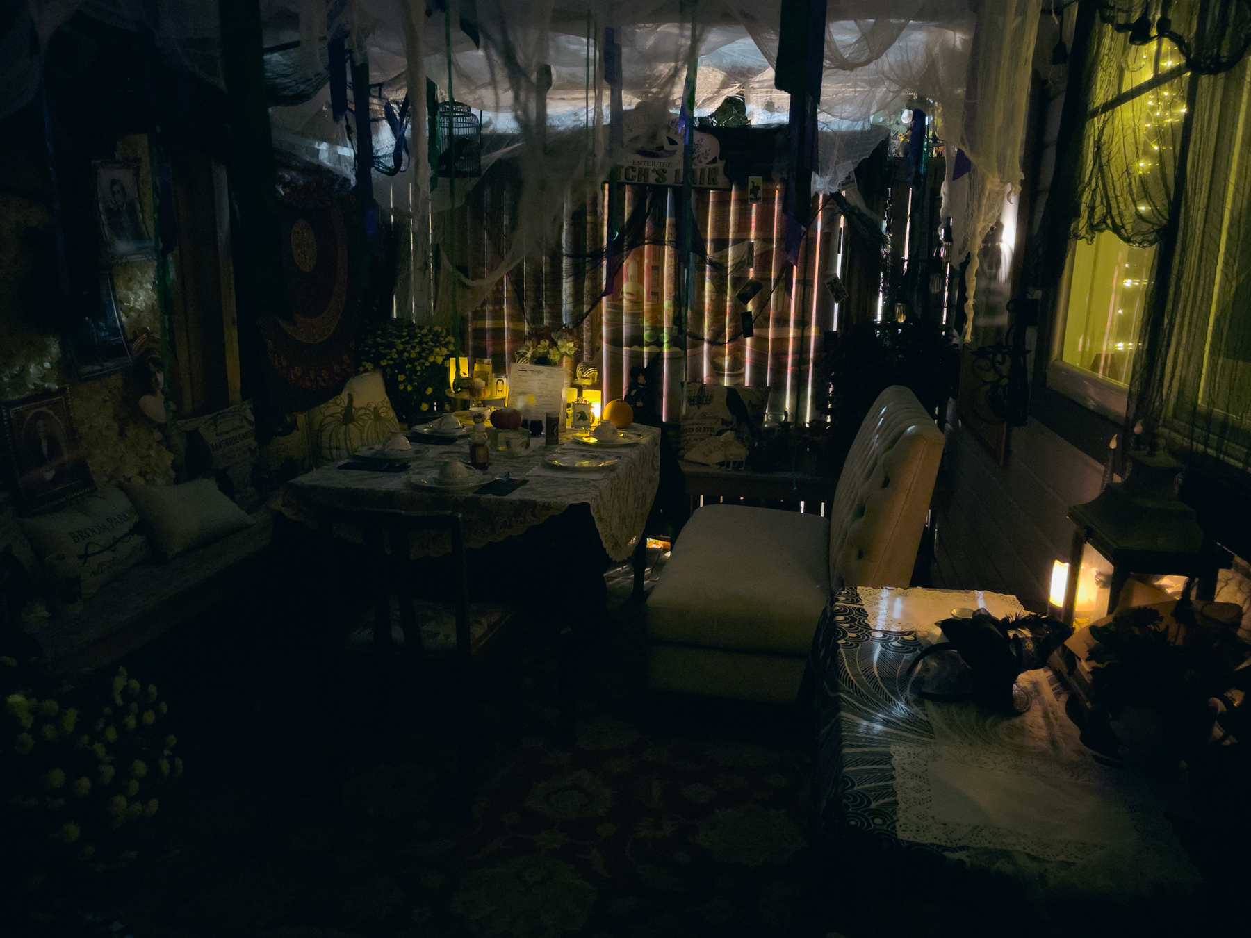 Dining table and chairs under an arbor at night illuminated by various light sources.
