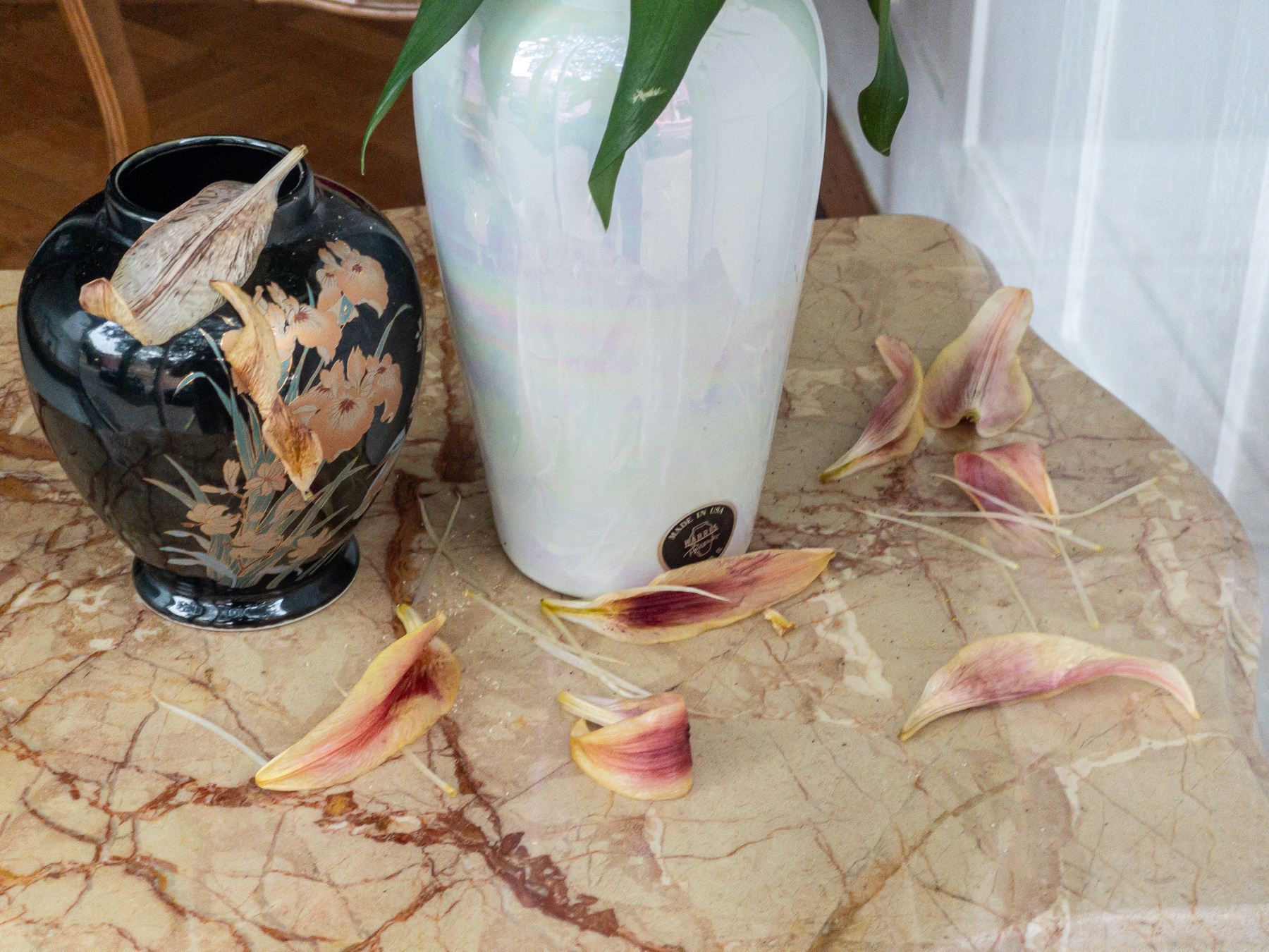 Lilly flower petals fallen on a marble table surface and a couple of vintage vases.