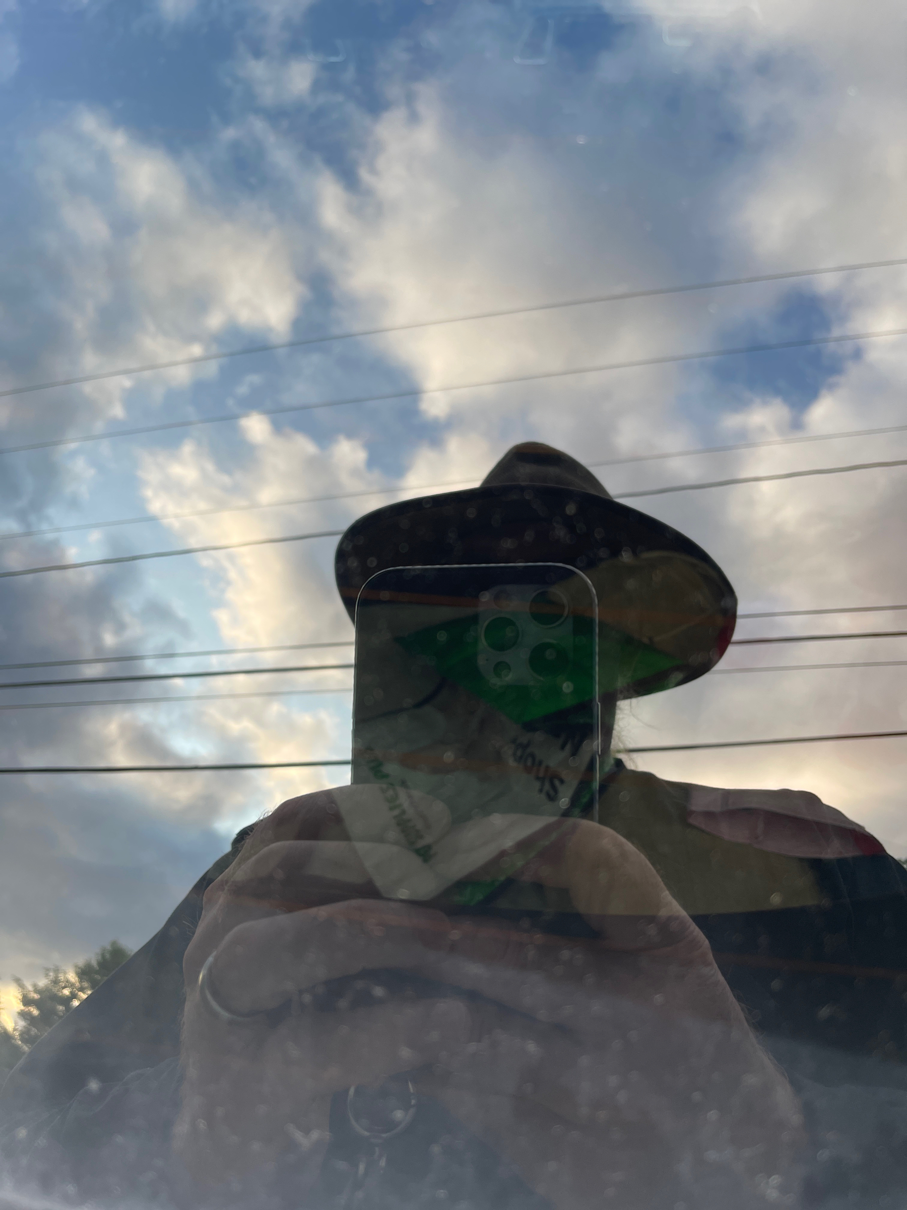 Self and clouds reflected in a car window.