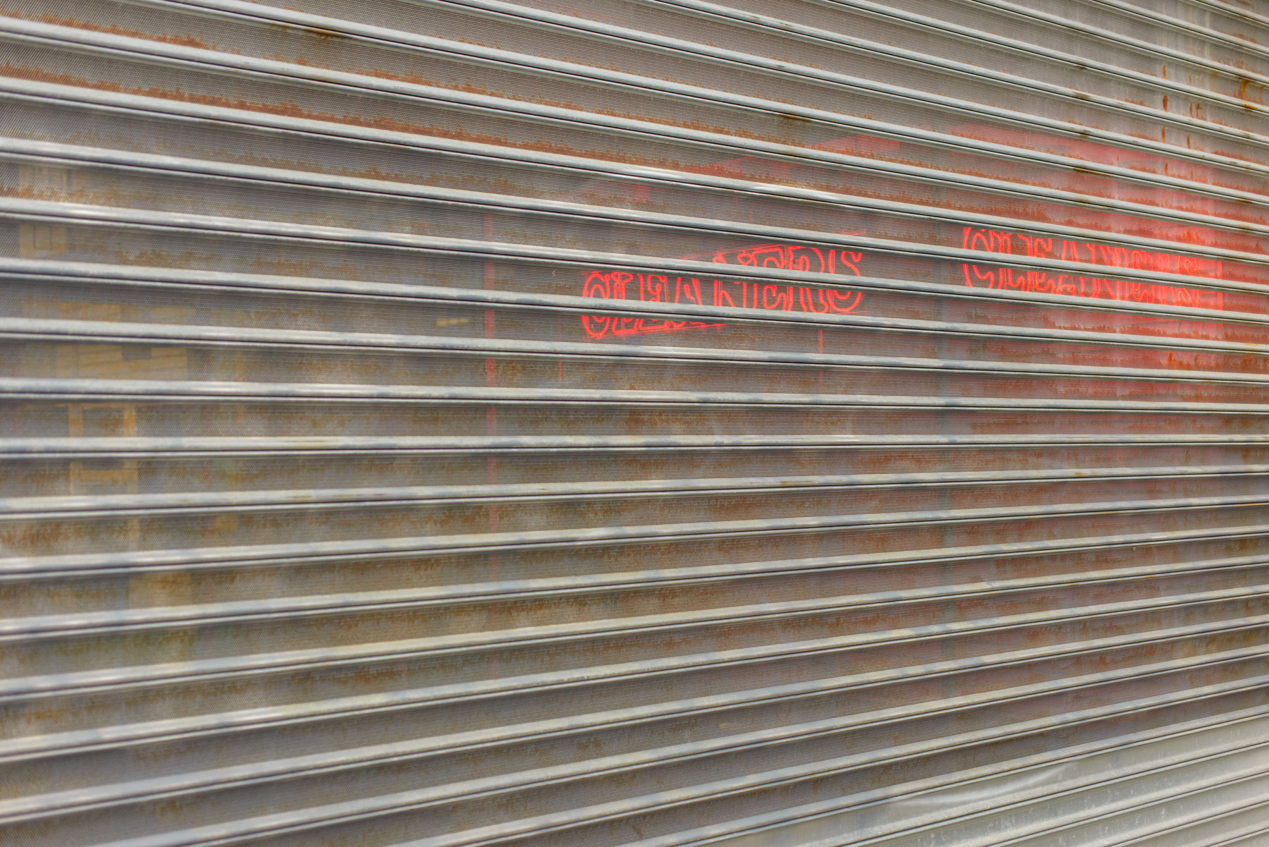 perforated security grille gate with neon “cleaners” signs shining through on the right side