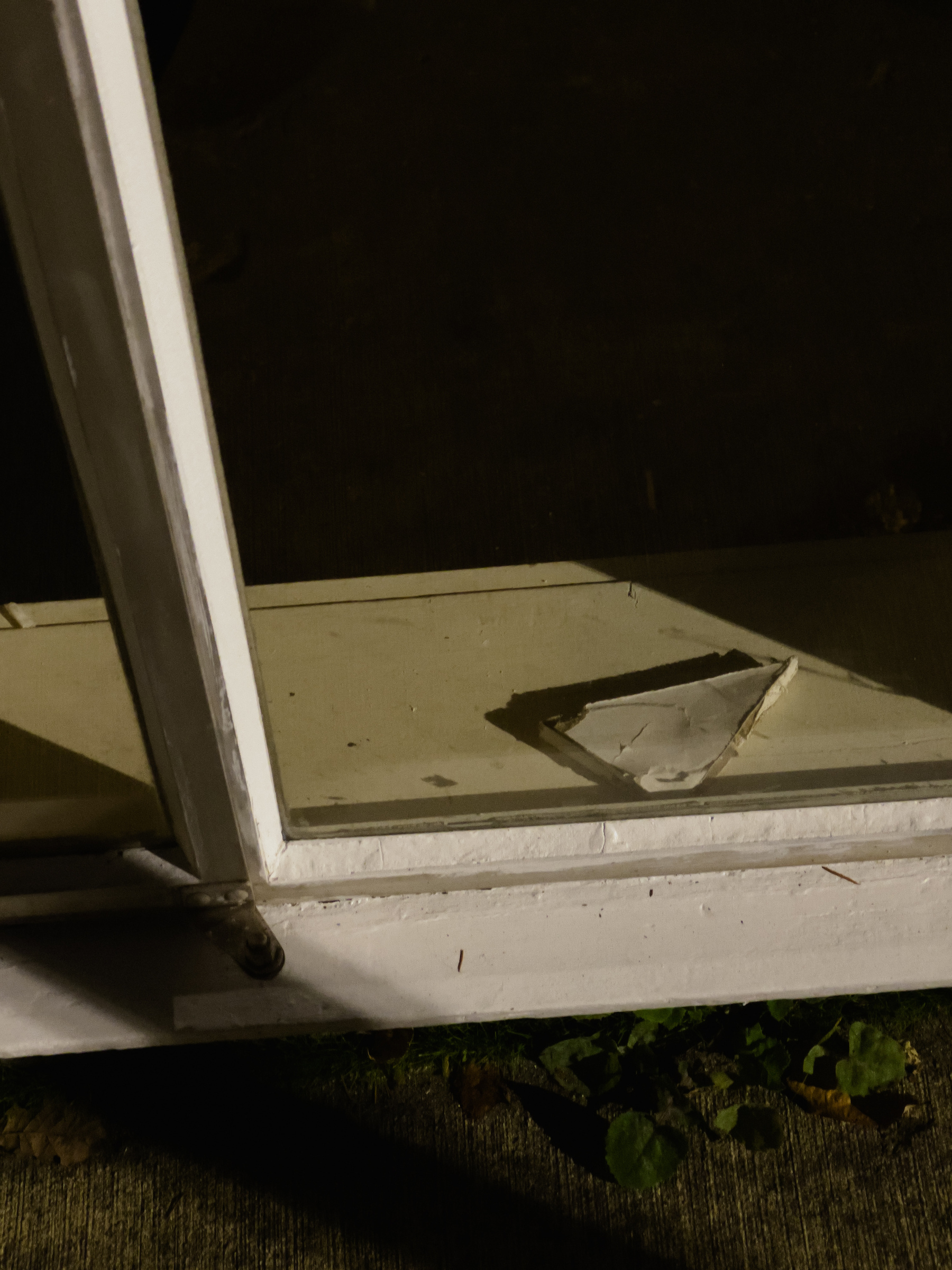Piece of thick broken glass on interior window sill at night illuminated by security lights outside.