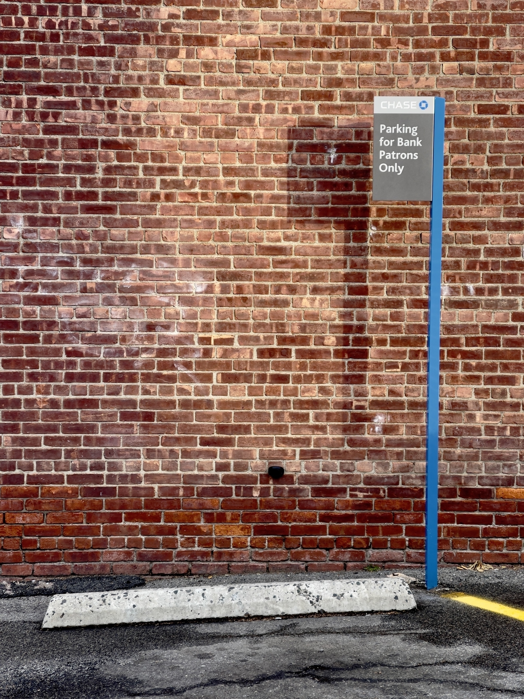 Brick wall, parking bumper, parking for bank patrons only sign.