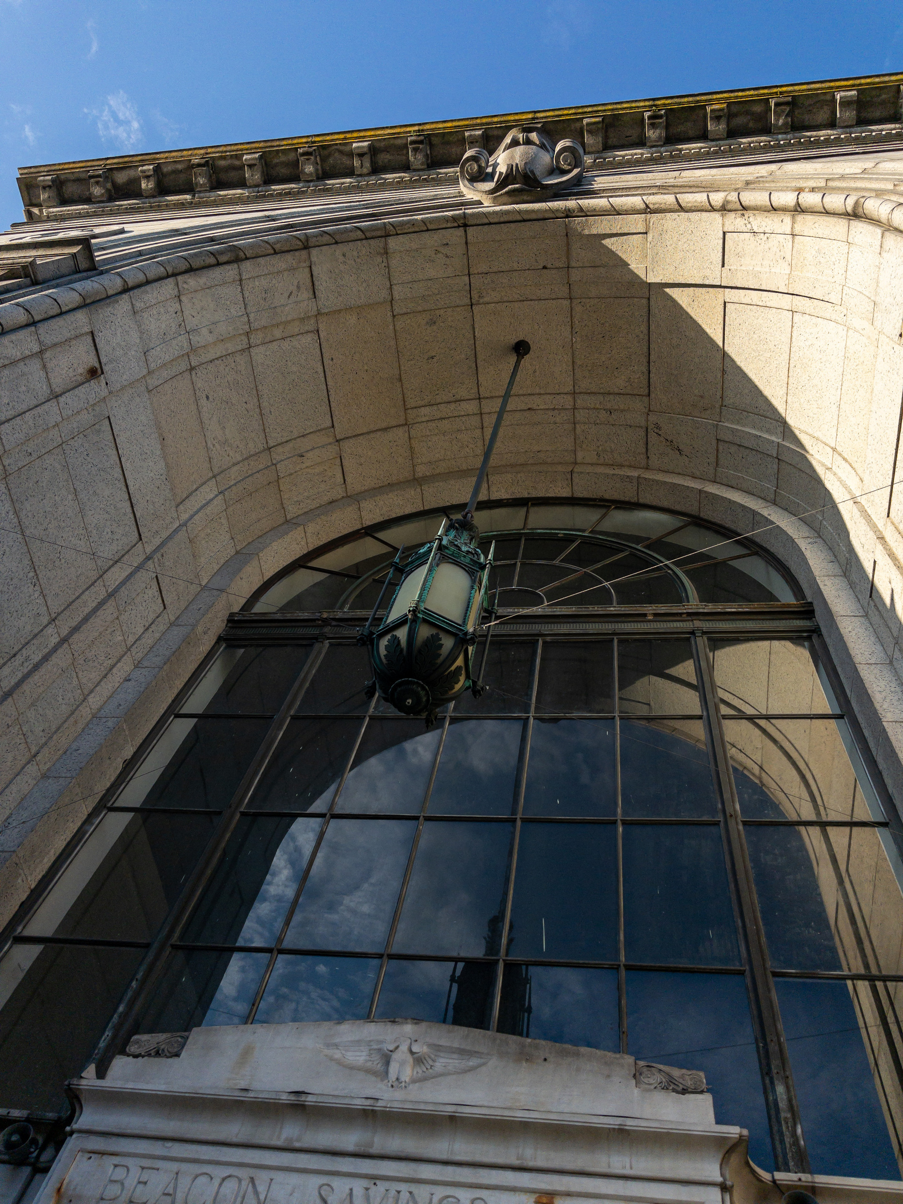 The arched recess and window of an old bank building from below looking up towards the sky.