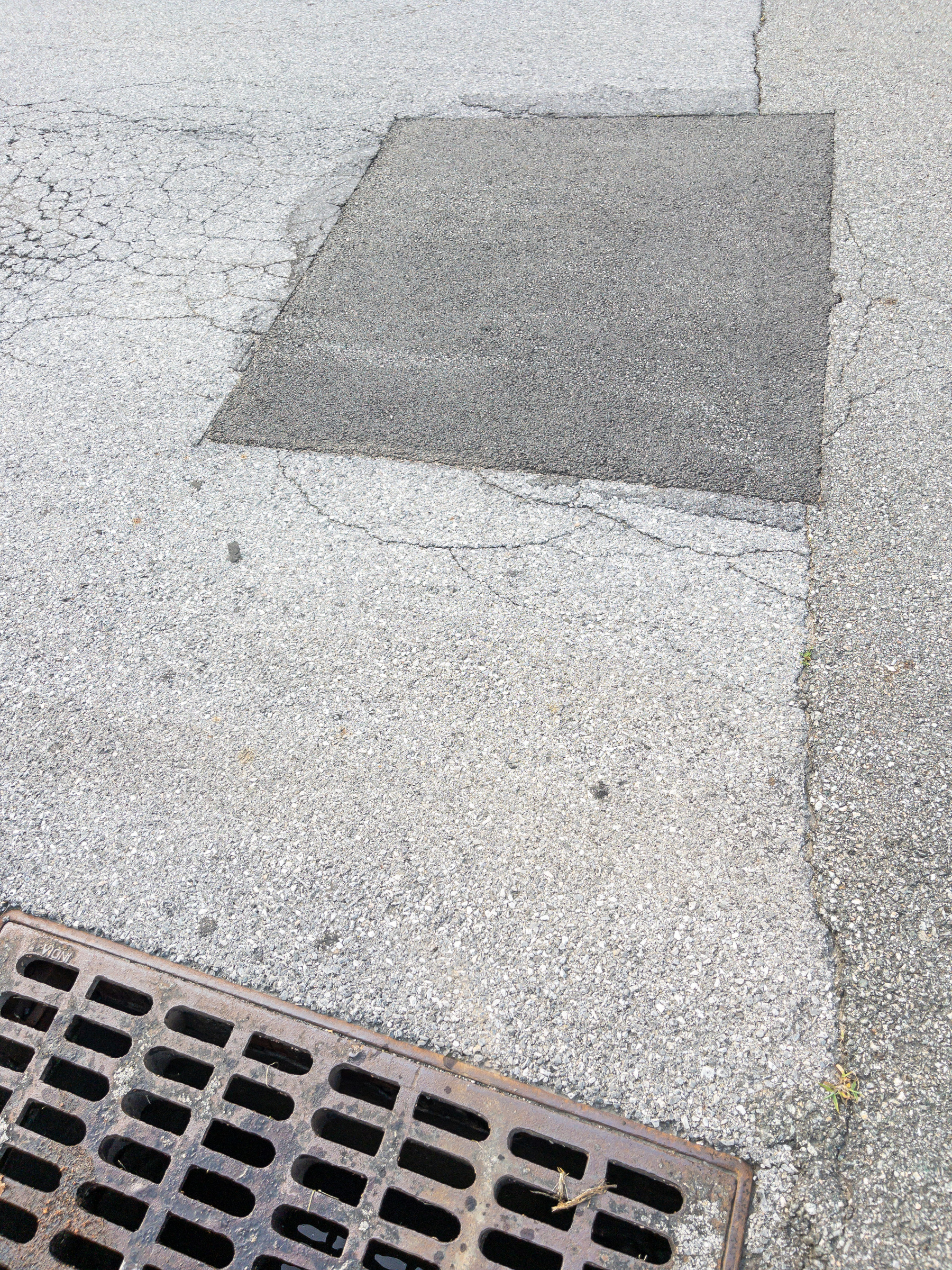 Rectangular patch in asphalt street surface. Drainage basin steel plate grid.