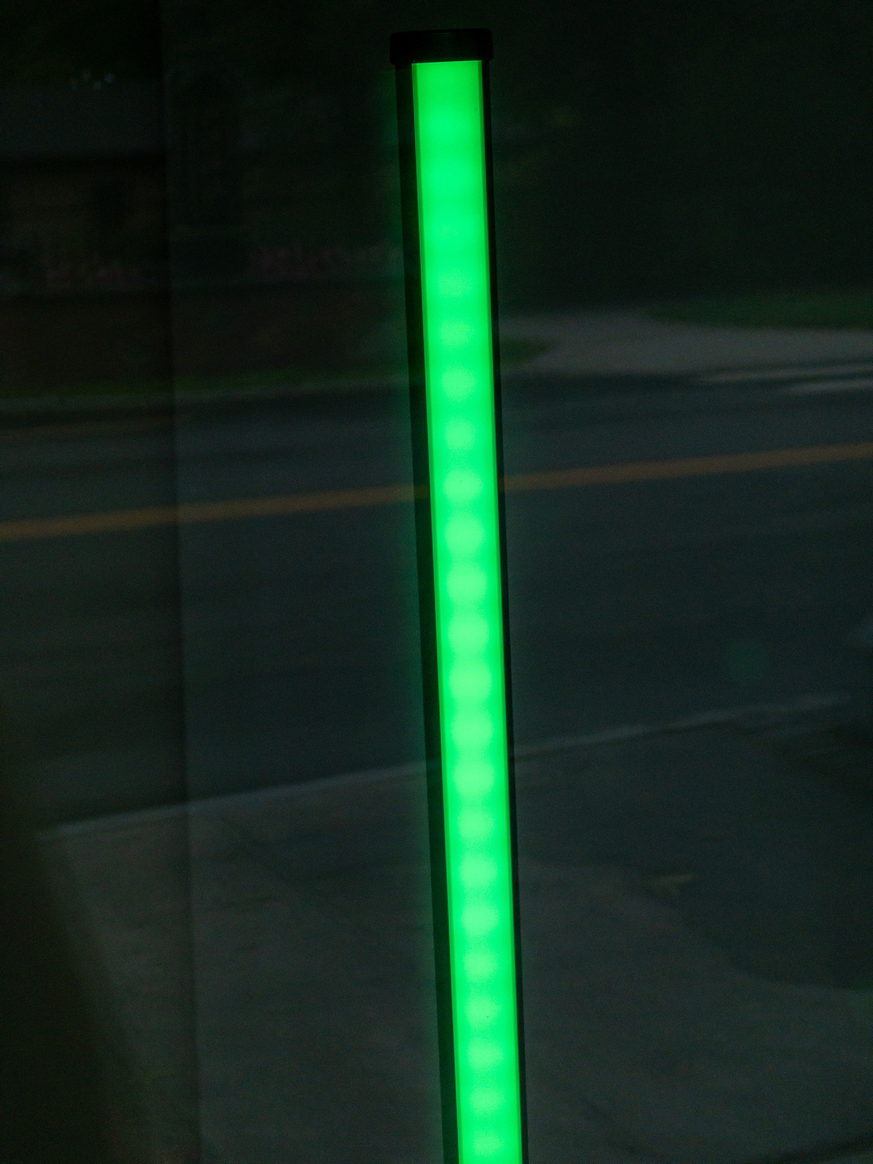 Green light tube in a shop window with reflection of street in the background.