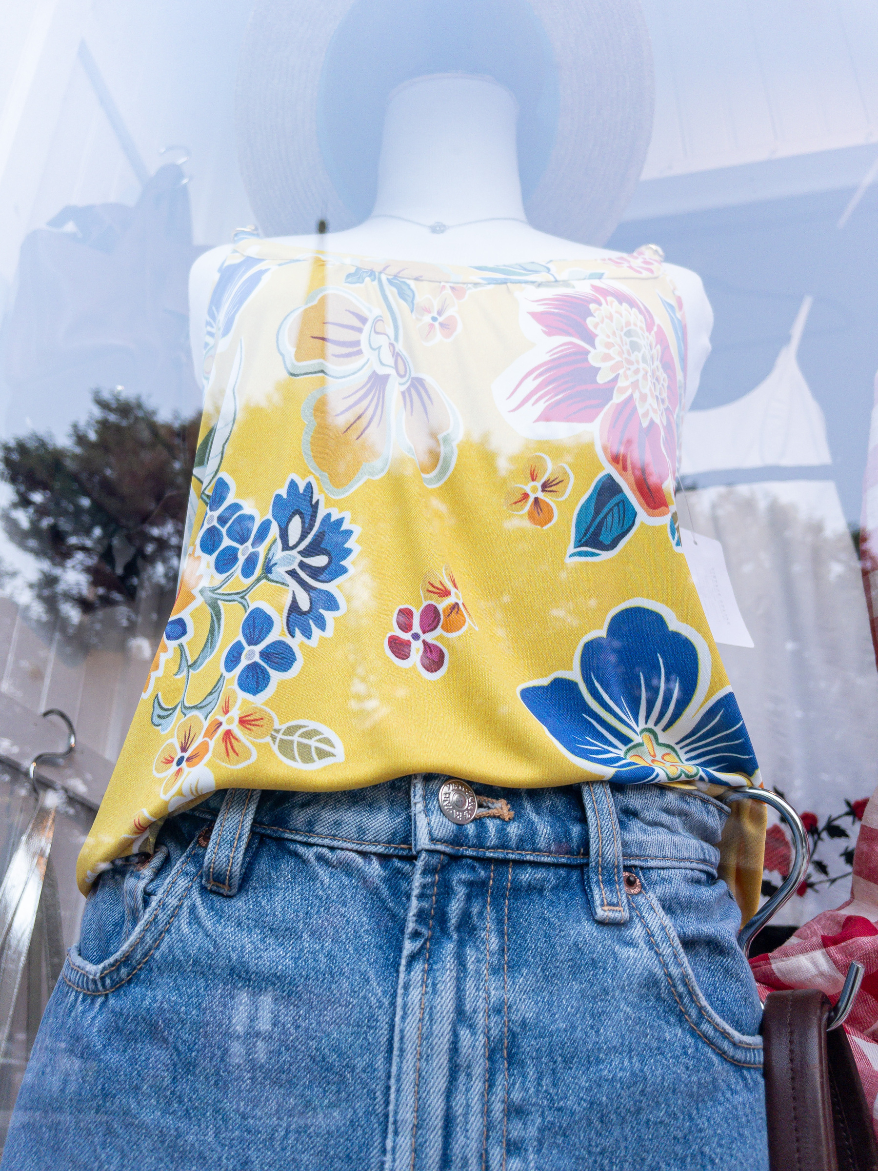Blue and yellow halter top, blue jeans, hat on a mannequin in a shop window.