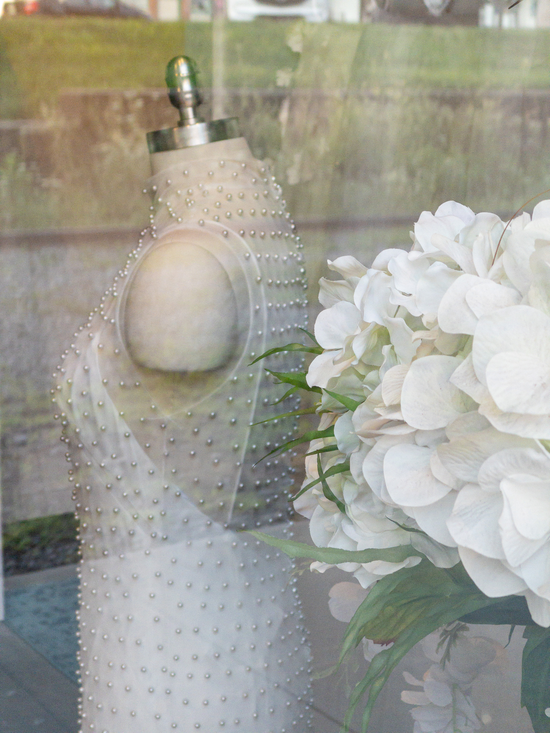 White hydrangea flower and torso mannequin with beaded white dress on it in a shop window.
