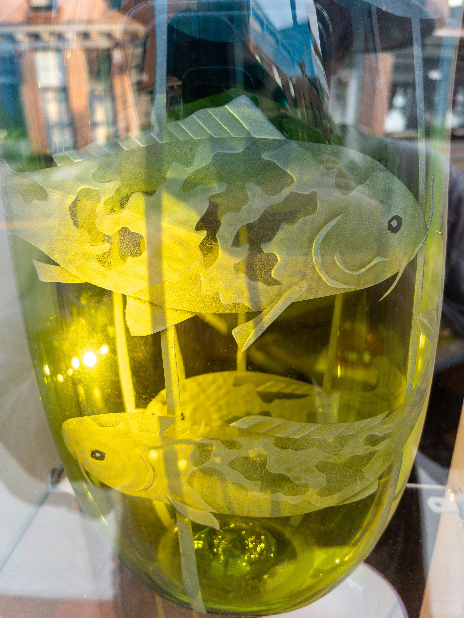 Yellow vase with carp etched into the sides in a shop window.