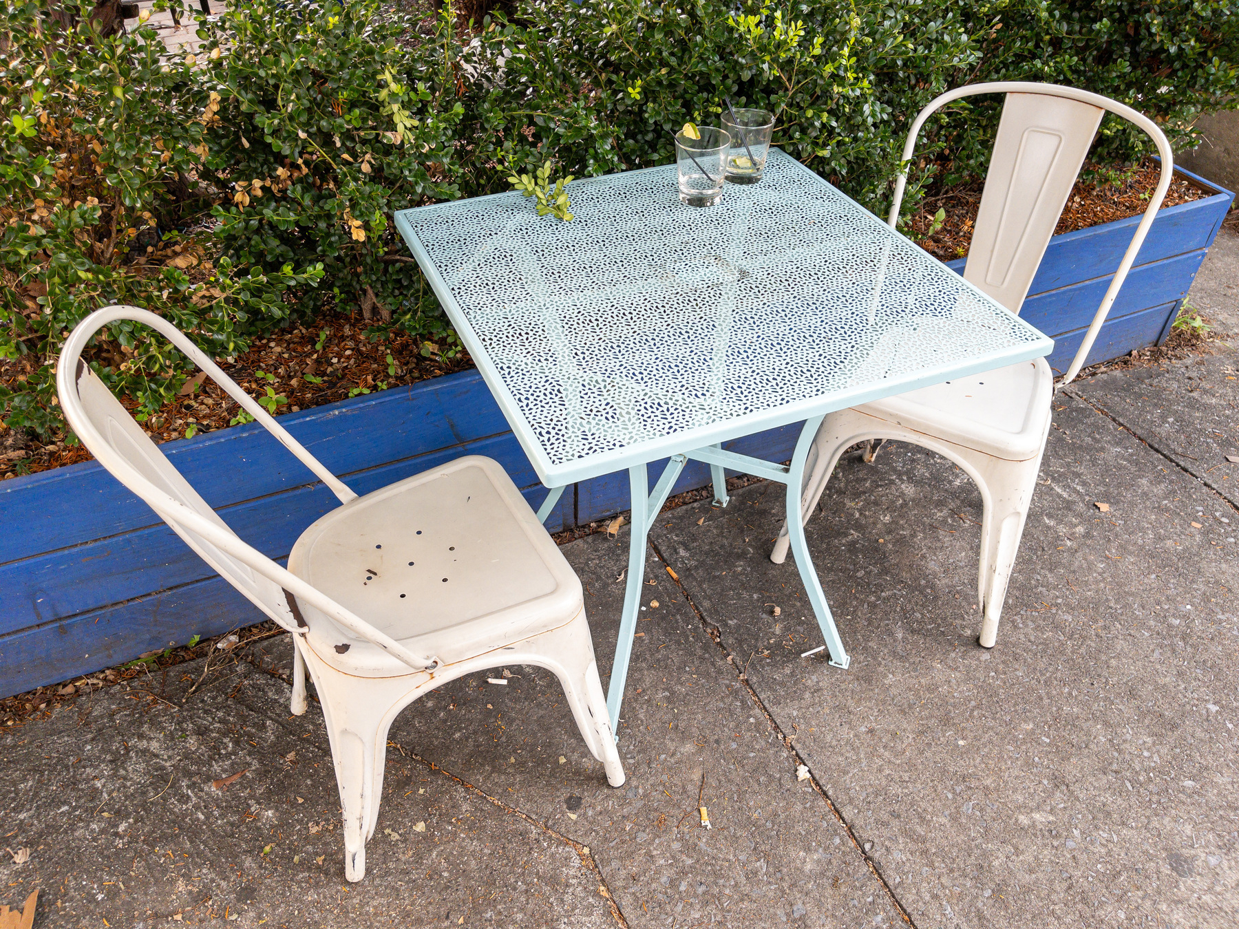 Metal table and chairs outside a drinking establishment with two glasses with partially finished drinks inside.