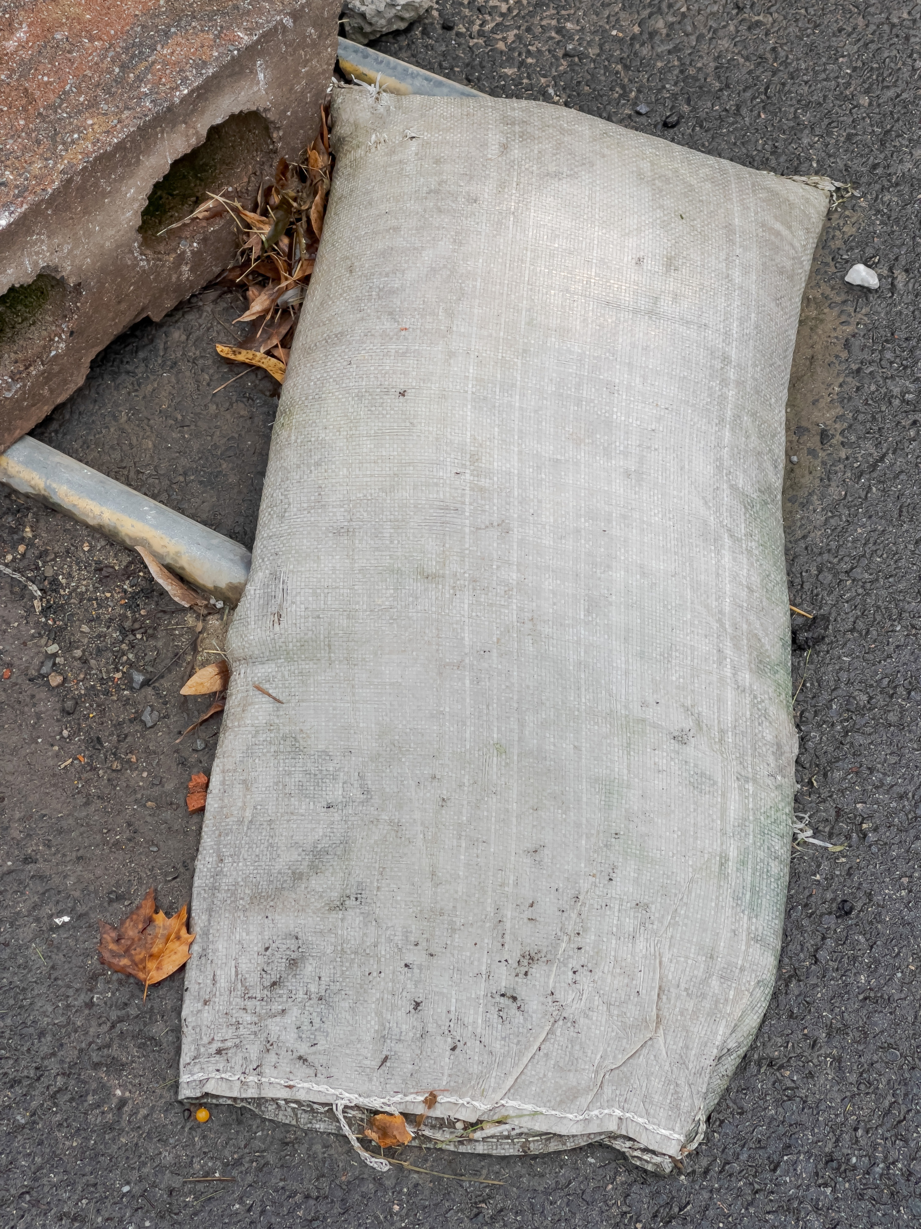 Sandbag laying on asphalt with concrete block in upper left corner of frame.