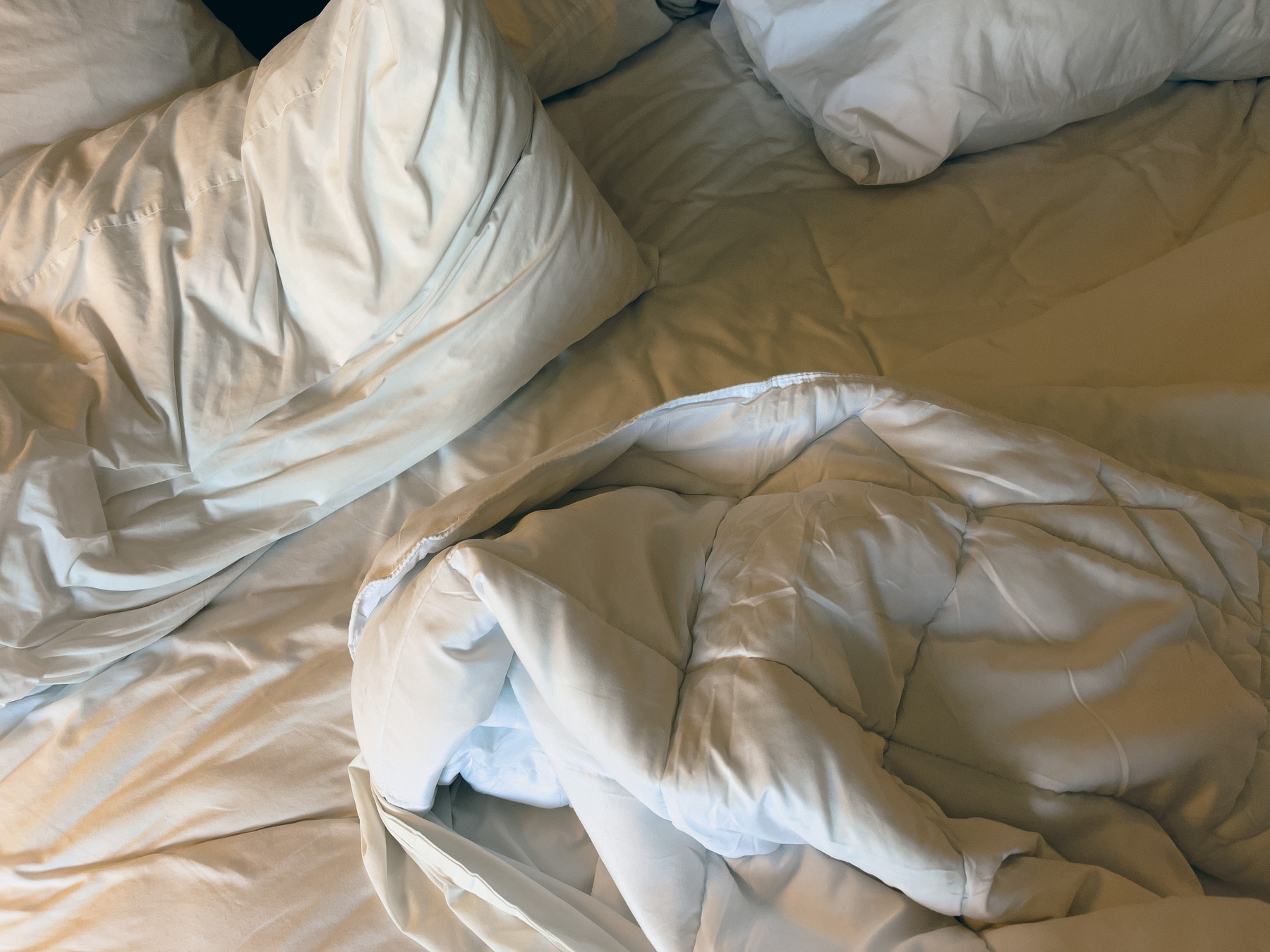 Closeup of rumpled pillows, blankets and sheets on a hotel room bed.