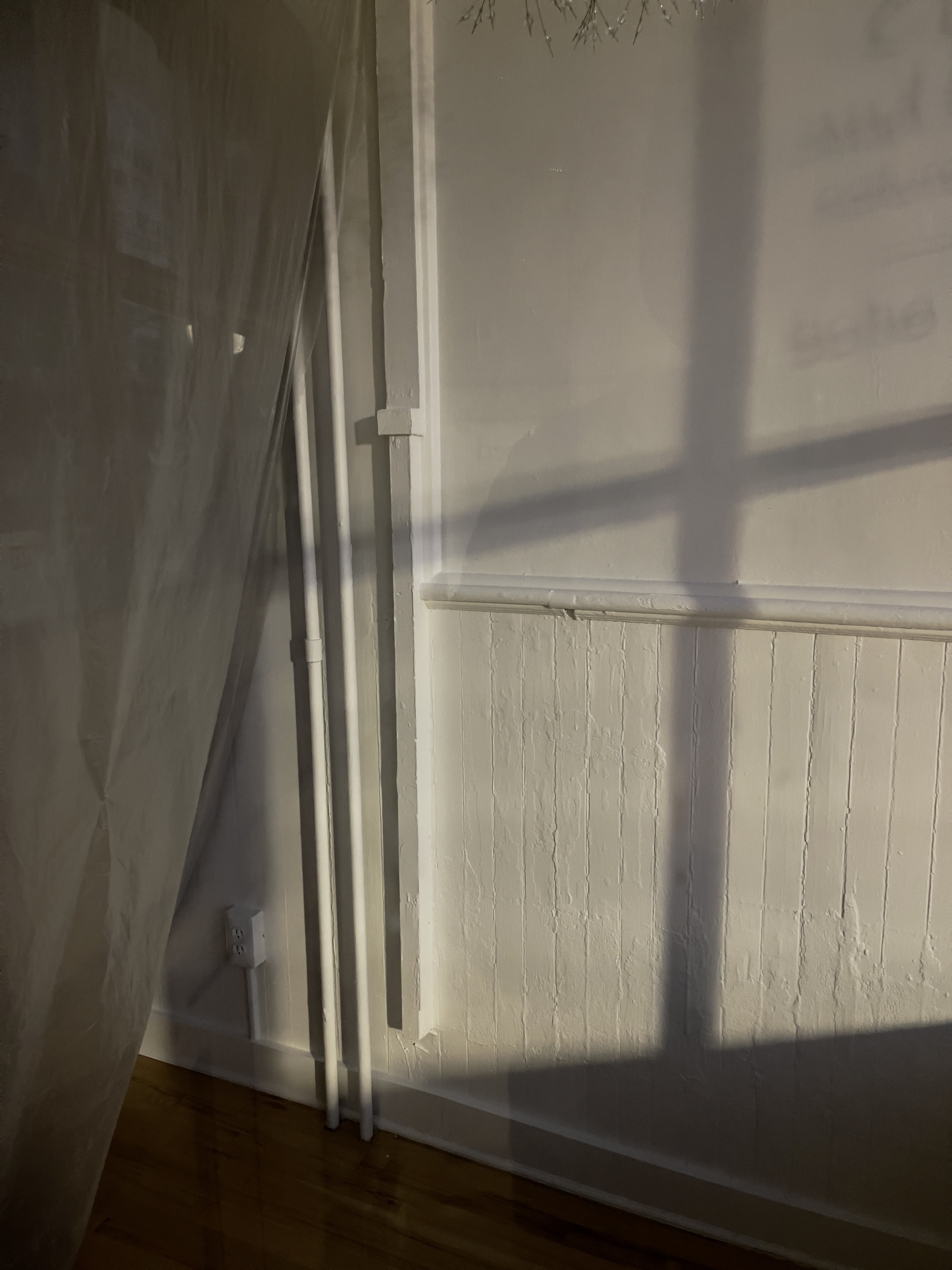 Shadow of window mullions cast across a wall with paneling and molding.