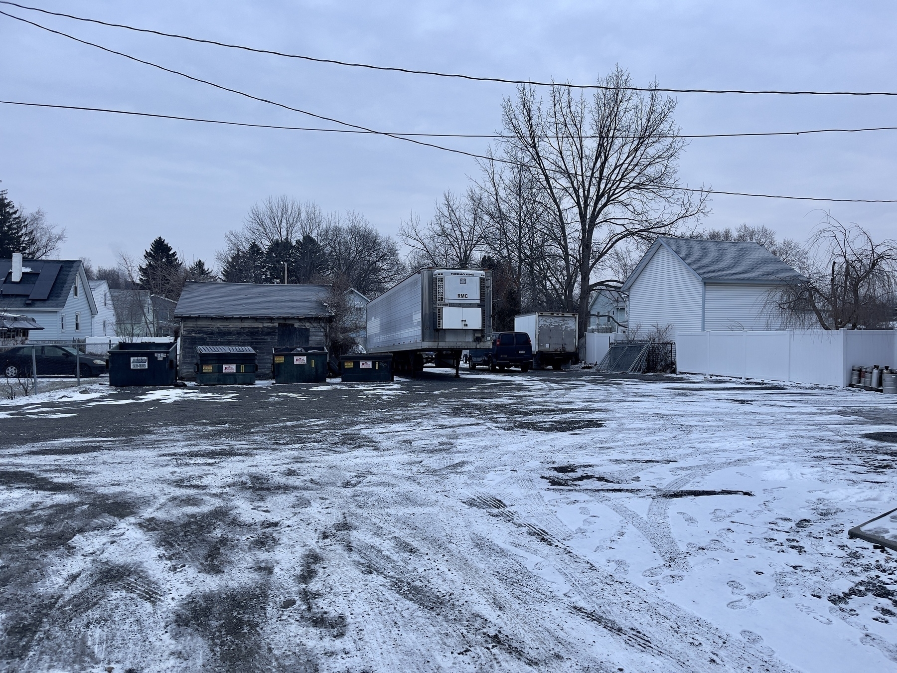 Parking lot wit small garage structures, garbage bins, truck and trailer.