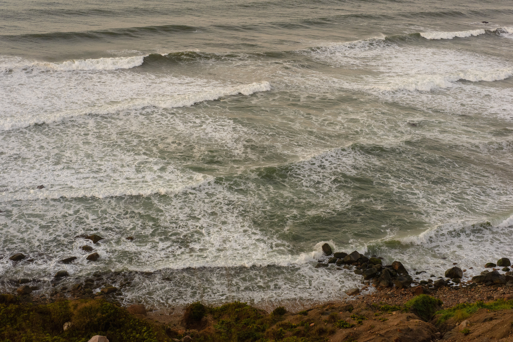 Ocean waves coming ashore from a bluff above.